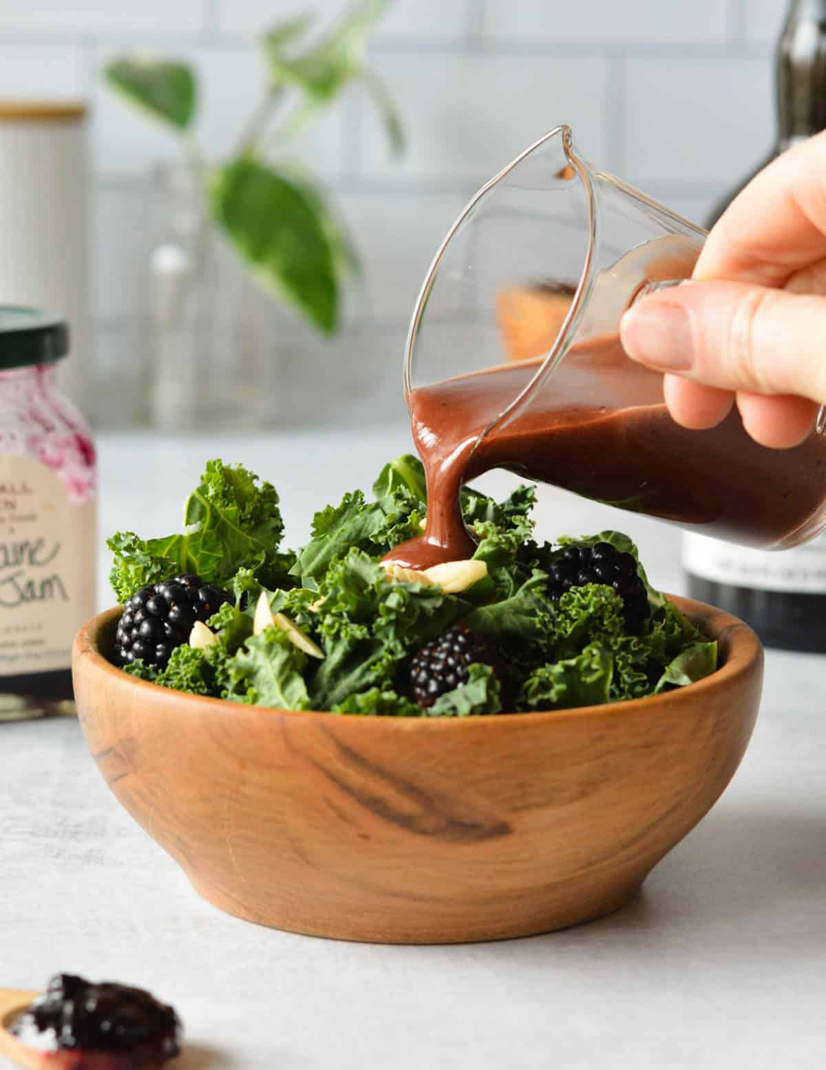 pouring balsamic dressing onto a kale salad with blackberries and almonds.