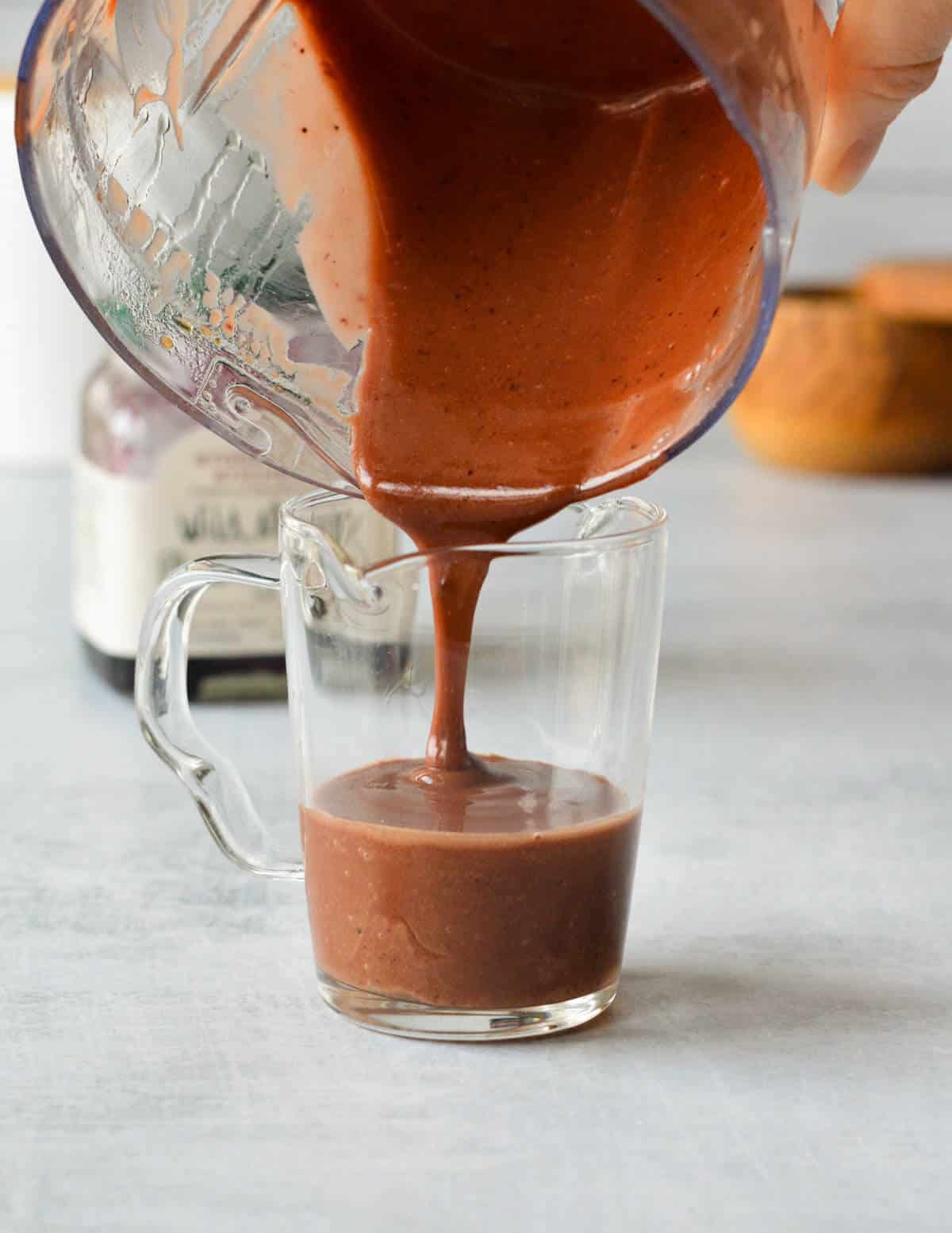 pouring balsamic dressing into a glass cup.