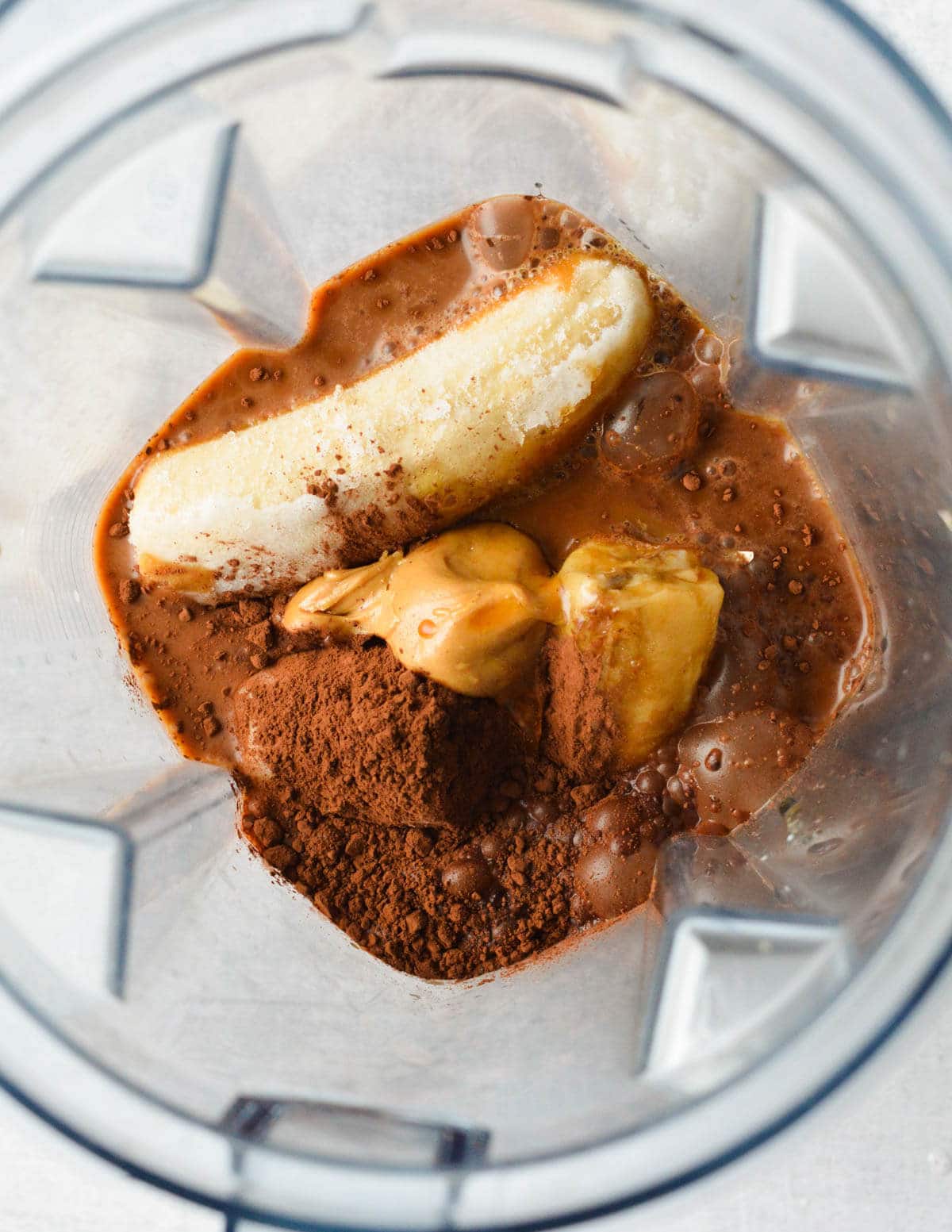 a blender with banana, peanut butter, coffee, cocoa powder, and milk in it.