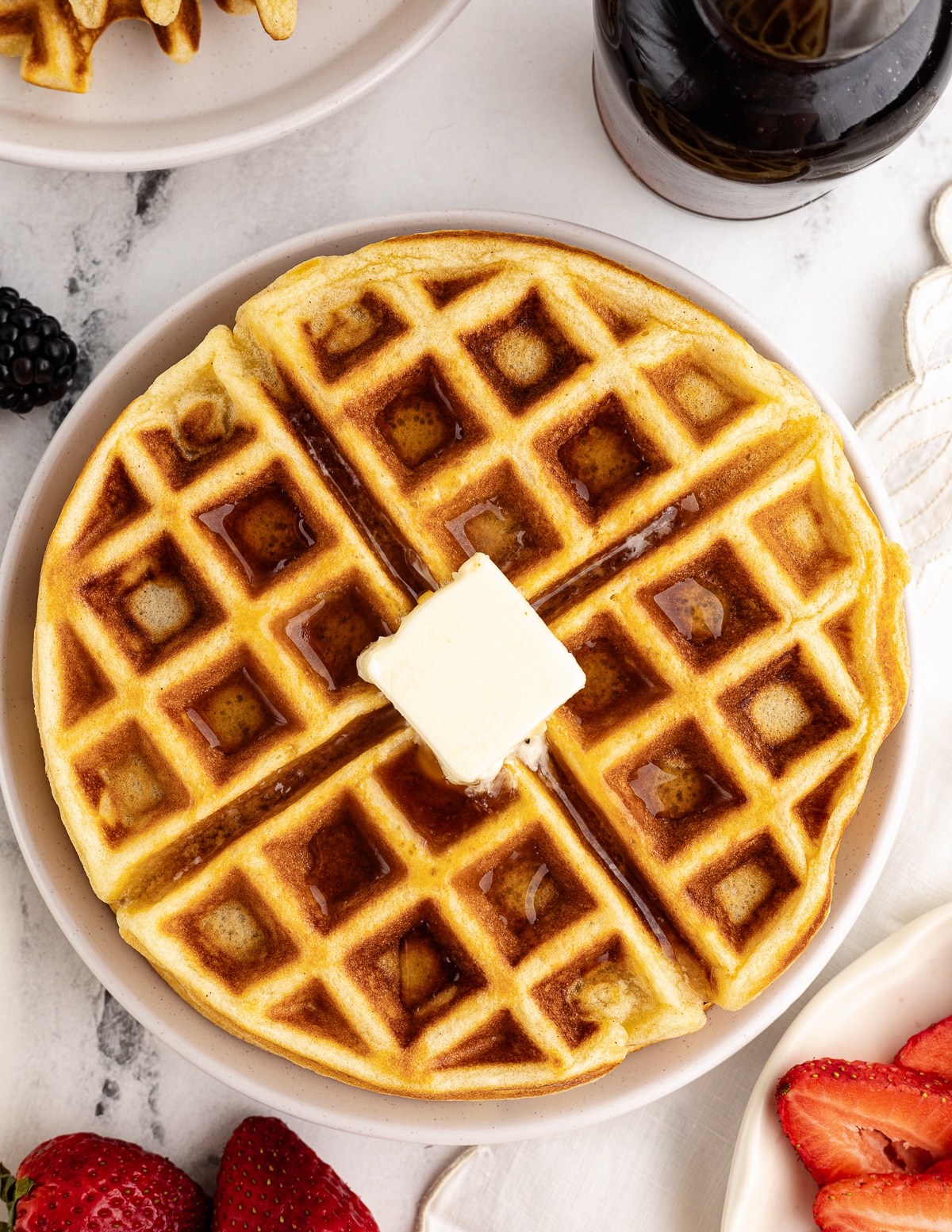 a gluten free waffle on a plate with a pat of butter in the middle.