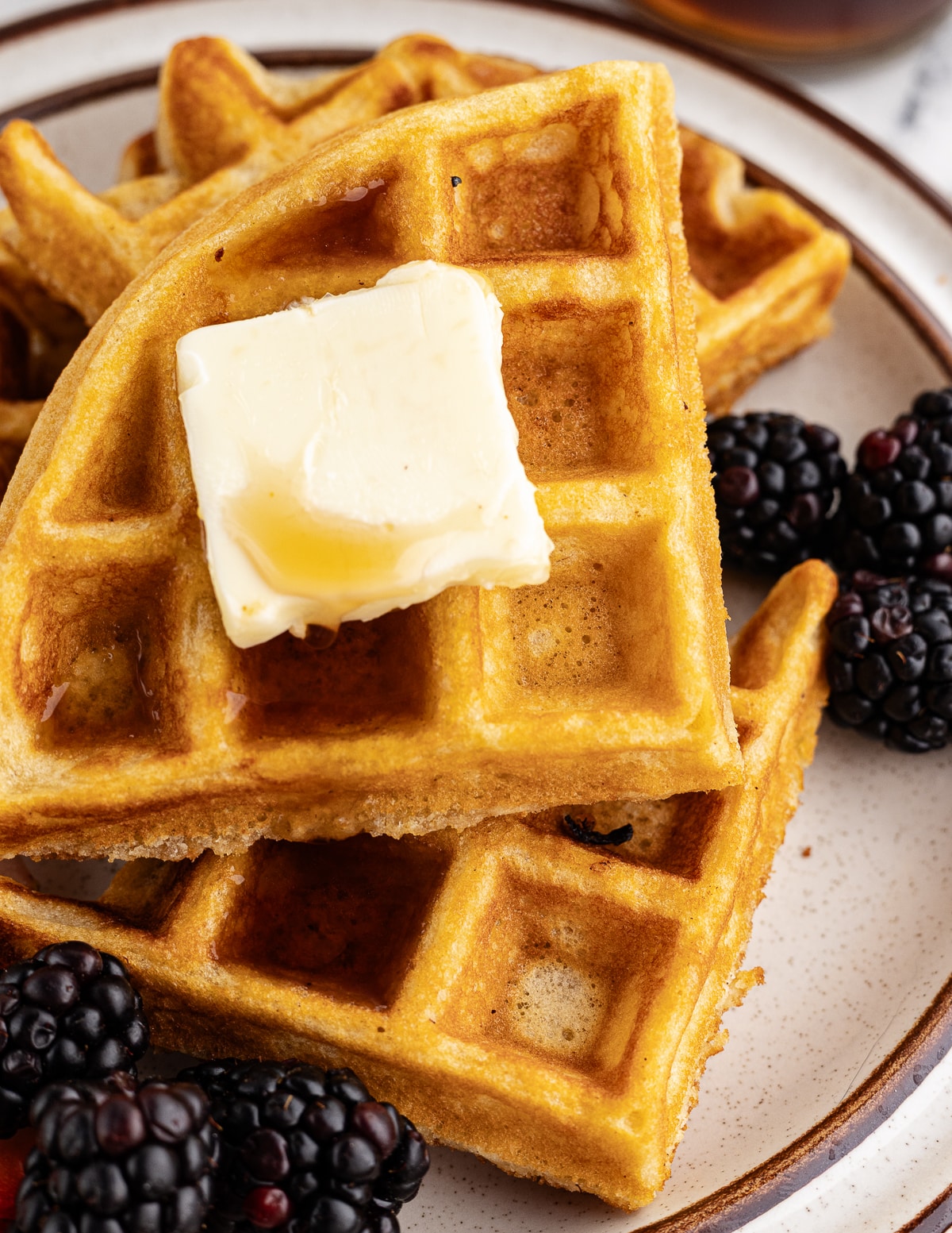 a stack of gluten free waffles on a plate with butter and syrup on top.