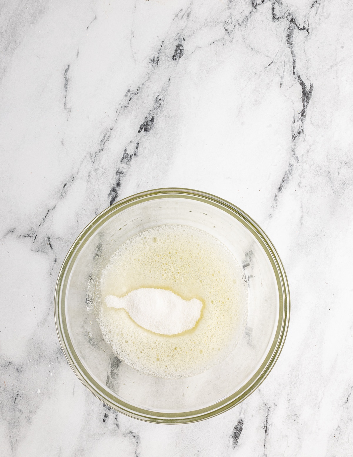 a bowl of frothy egg whites with sugar on top.