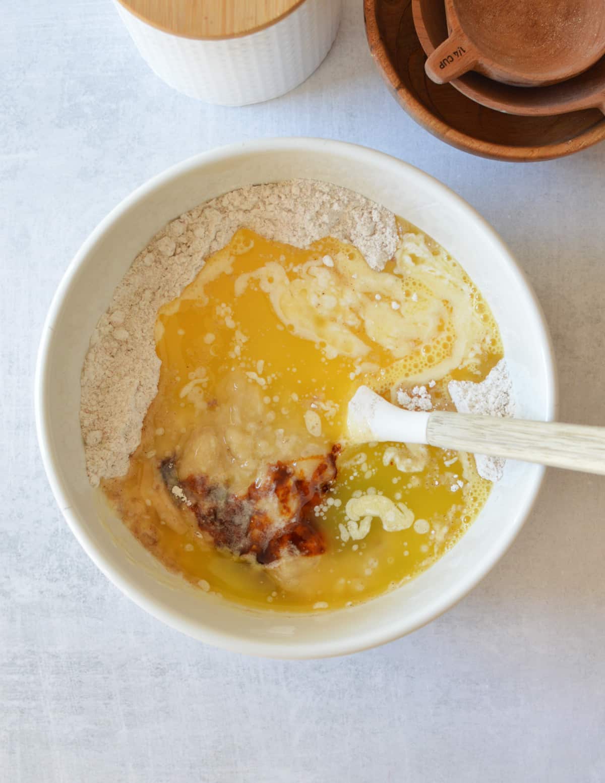 a bowl of gluten-free flour, sugar, melted butter, eggs, and mashed banana.