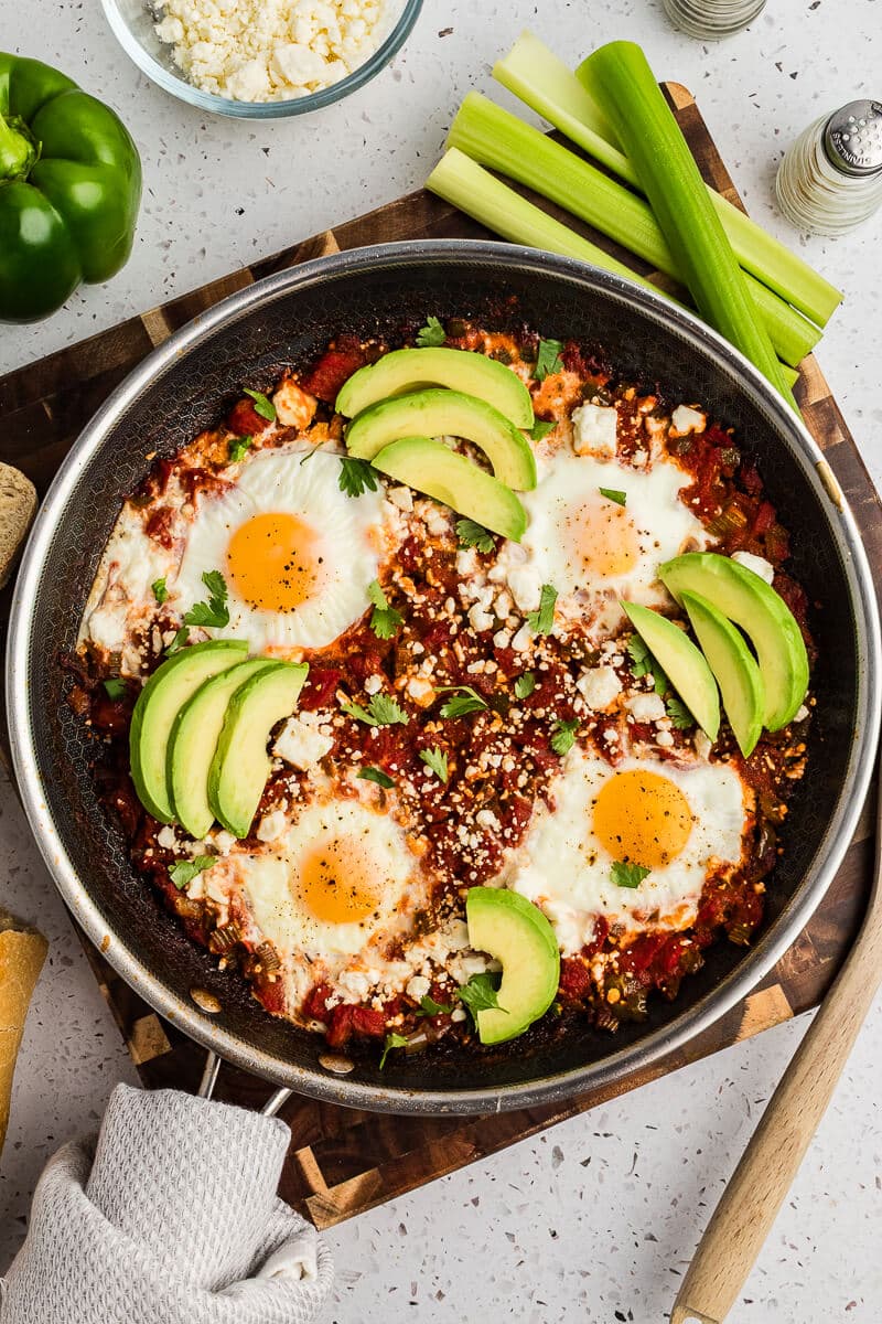 a skillet with shakshuka with eggs cooked in a tomato sauce with feta and avocado on top.