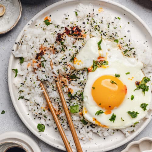 a plate of white rice with a fried egg and chili oil on top.
