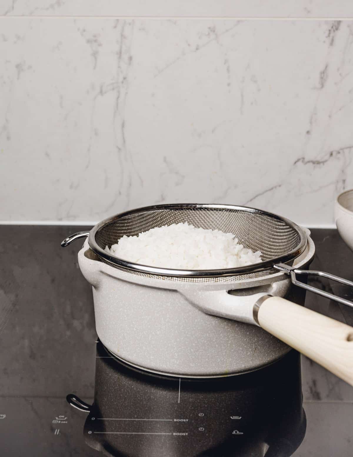a strainer full of cooked rice set in a saucepan.