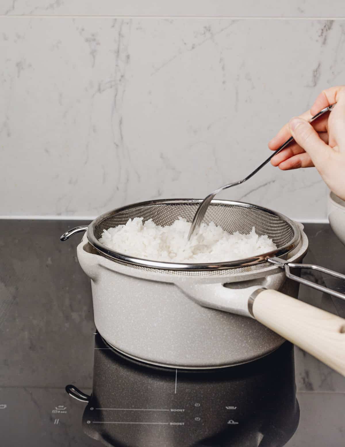 fork fluffing cooked rice in a strainer with a fork.