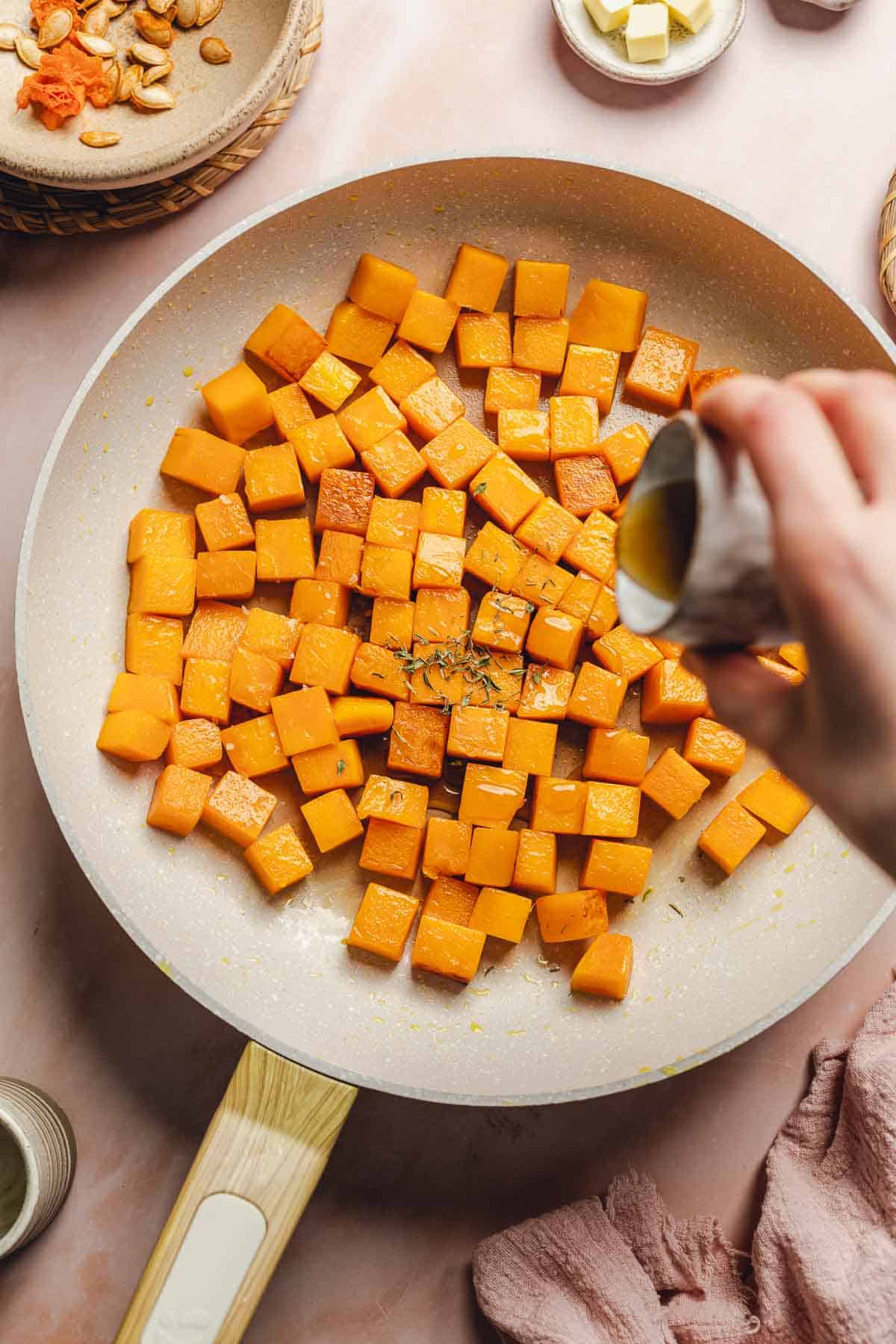 pouring maple syrup into a skillet with butternut squash.