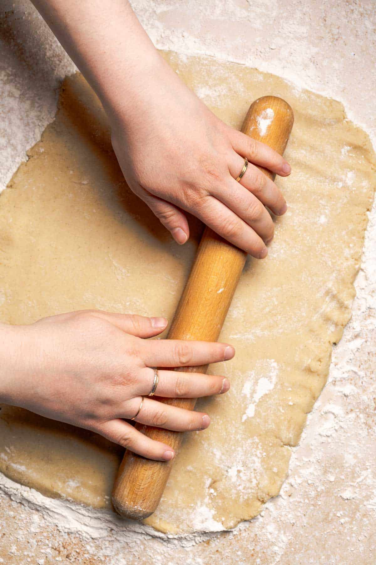 hands using a rolling pin to roll out gluten free cinnamon roll dough.
