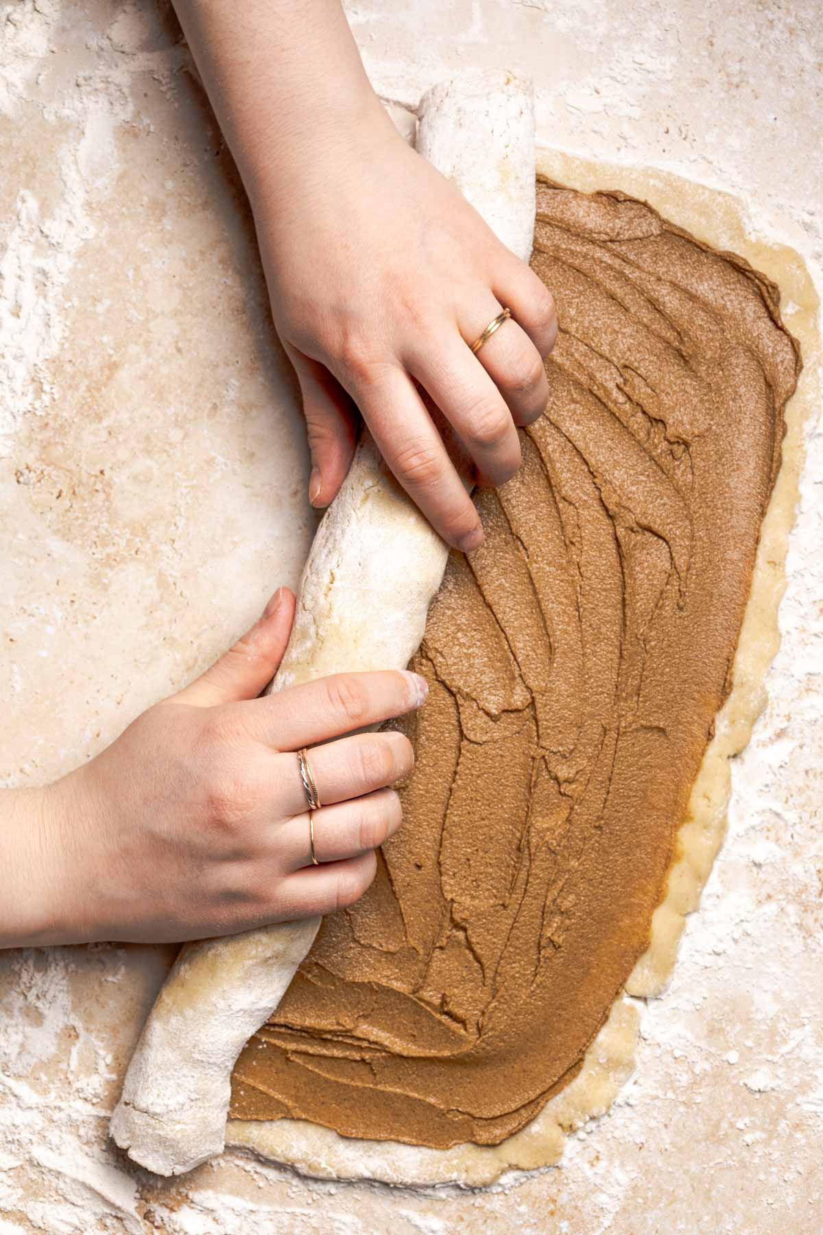 hands rolling up gluten free cinnamon roll dough into a log.