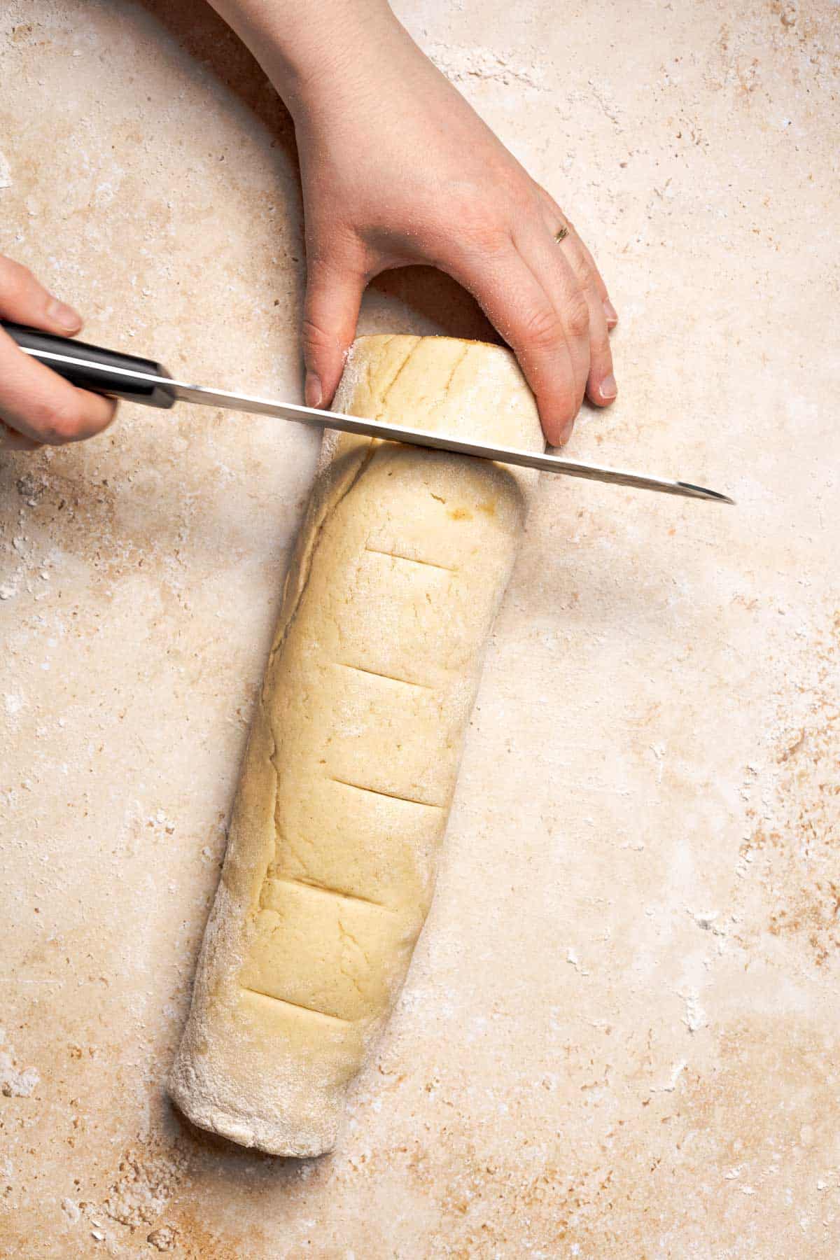 hand holding a knife on top of a dough log about to cut into it.