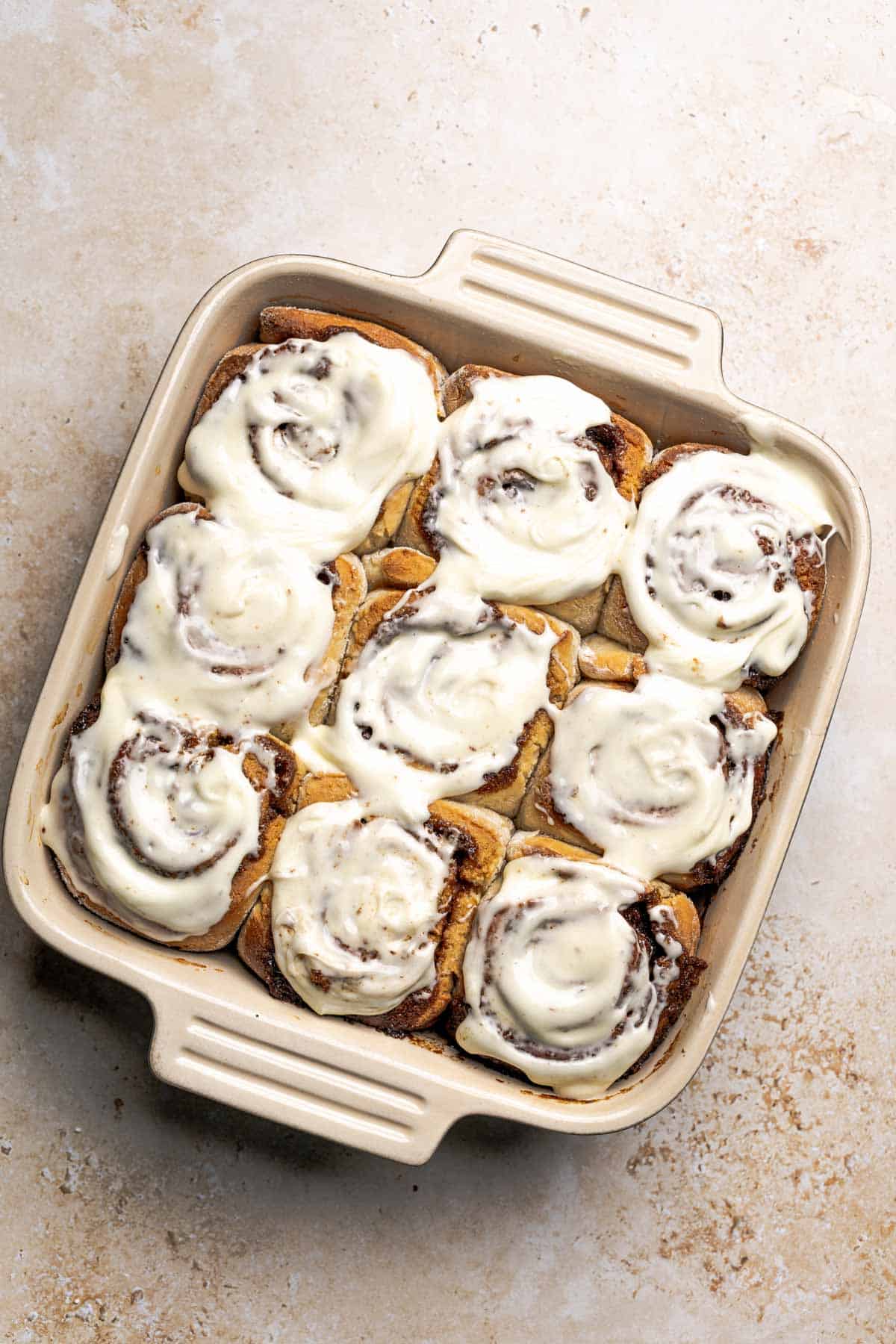 a pan of baked cinnamon rolls with cream cheese frosting on top.
