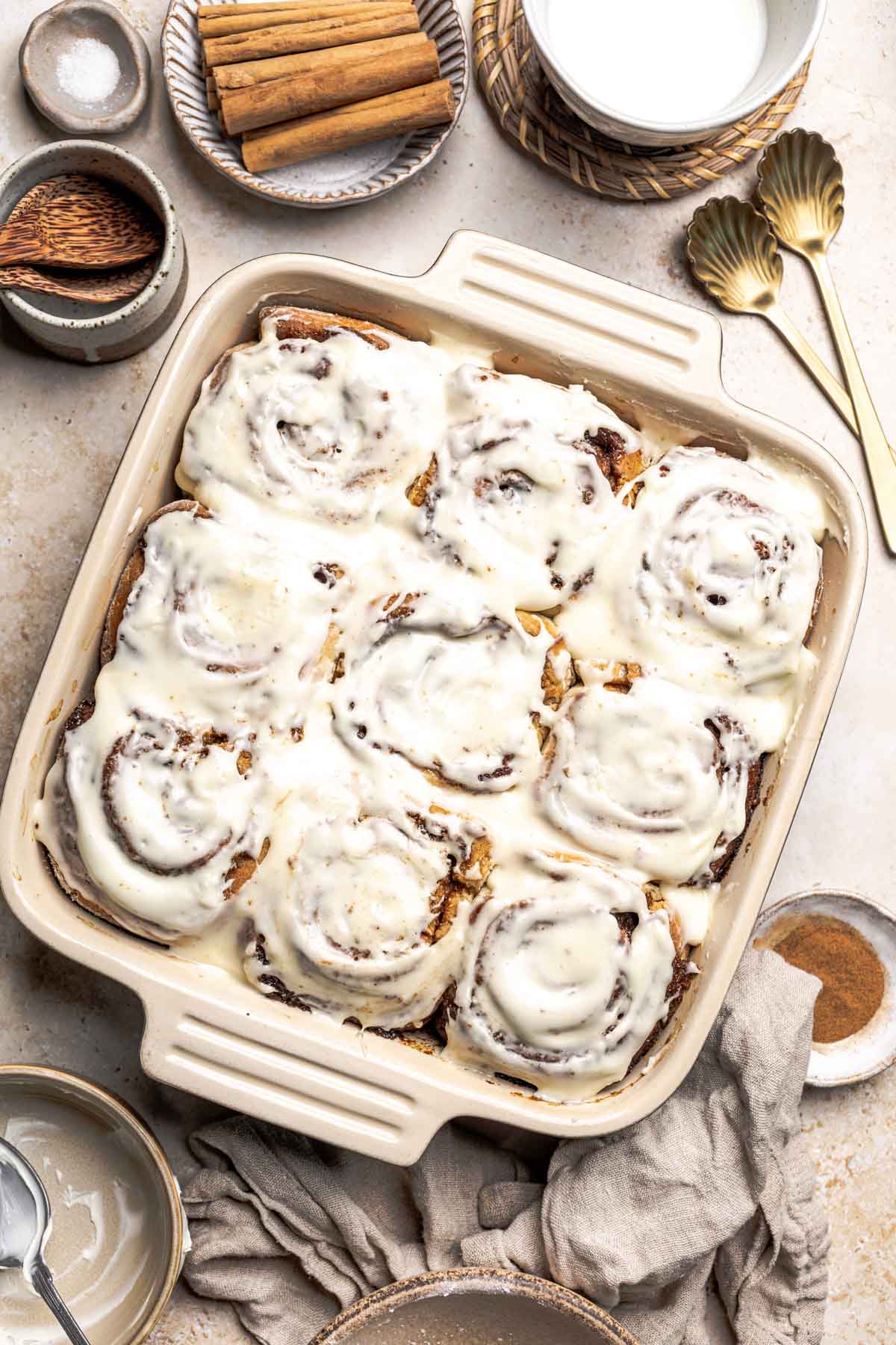 a baking dish with homemade gluten free cinnamon rolls with cream cheese frosting on top.