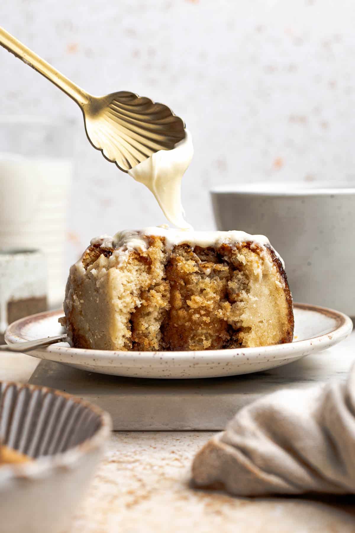 spoon drizzling cream cheese frosting onto a cinnamon roll.
