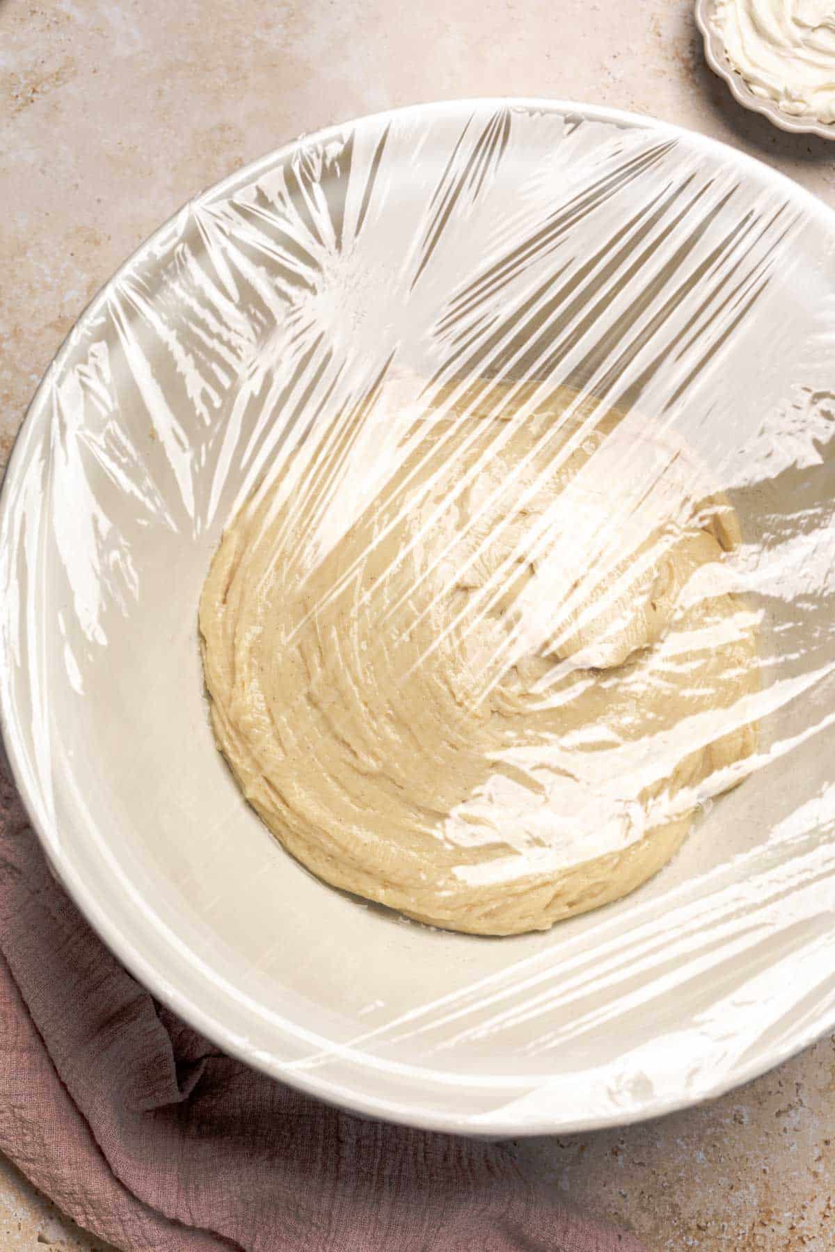 gluten free dough in a bowl covered with saran wrap.