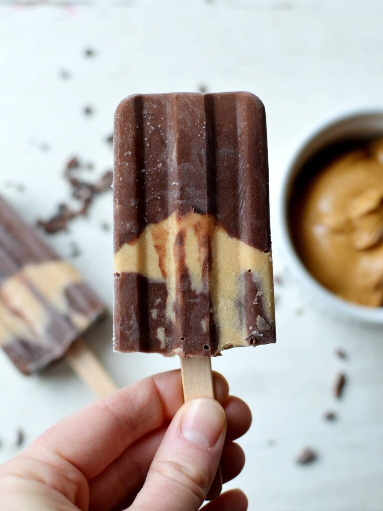 close up of a banana popsicle with chocolate and a peanut butter layer