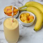 A banana peach smoothie with fruit behind it