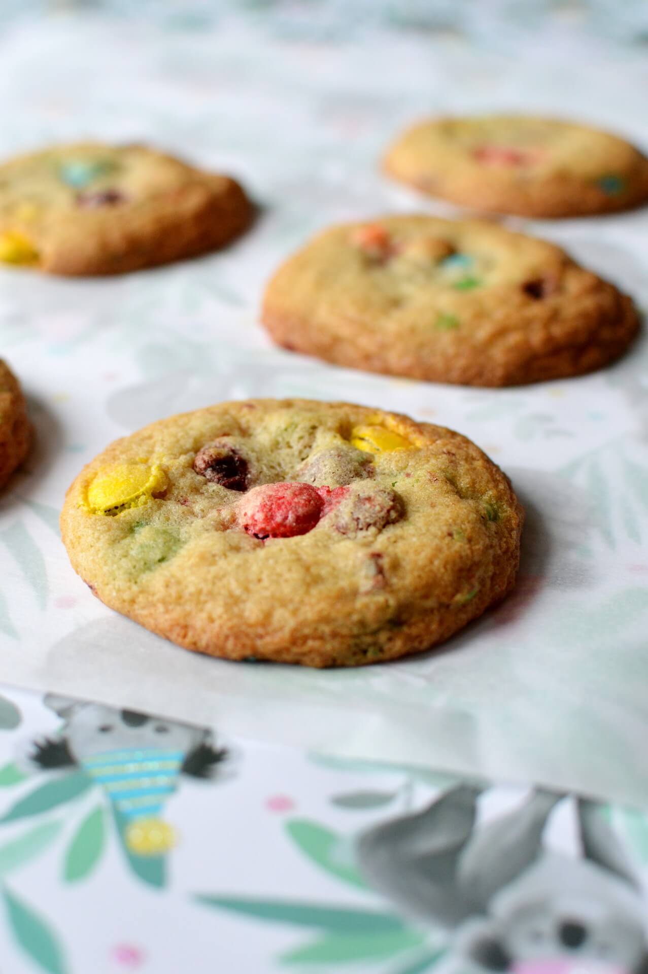 Five gluten free M&M cookies laying on a piece of parchment paper.