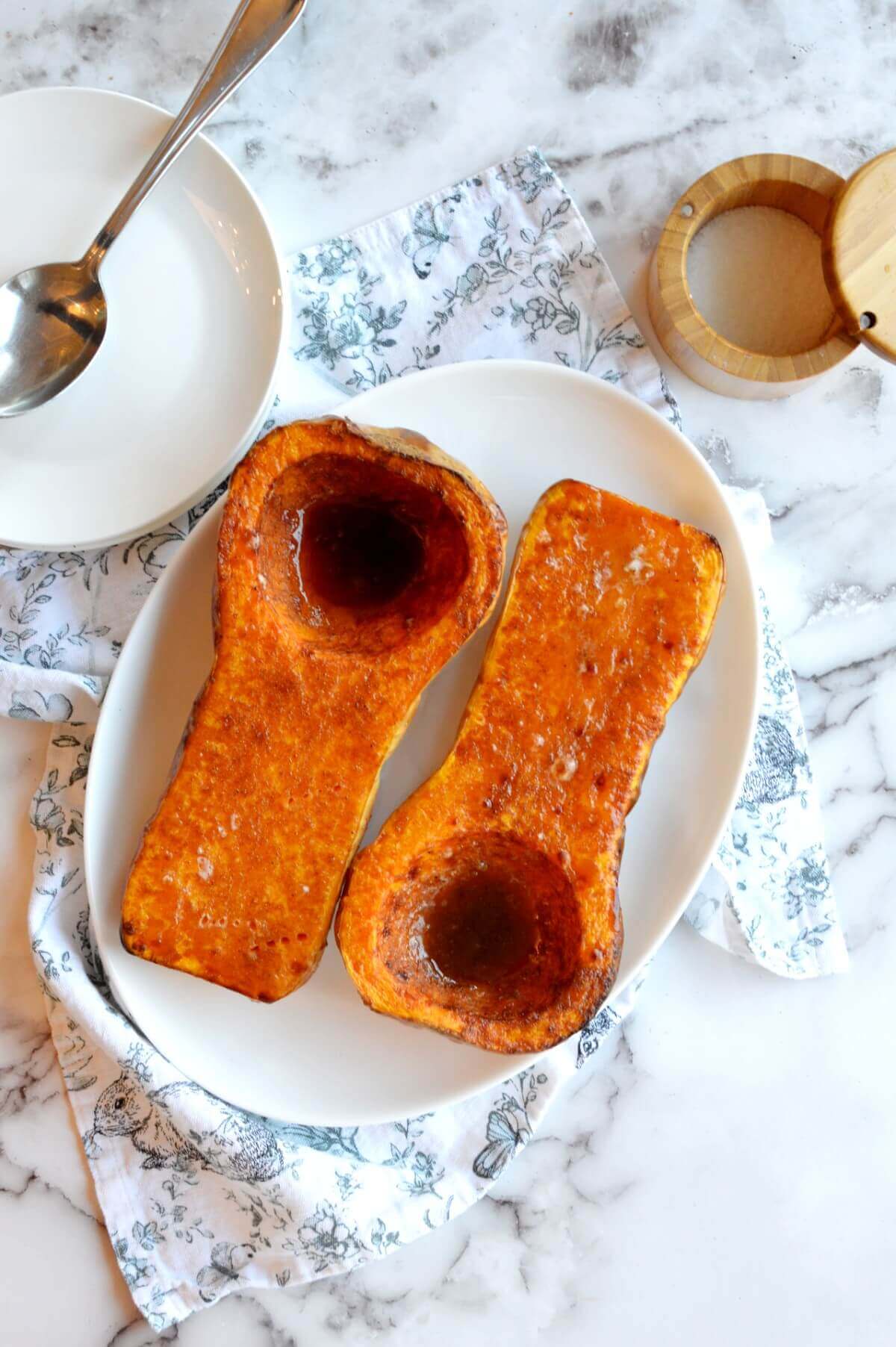 Two butternut squash halves on a plate that are roasted with brown sugar