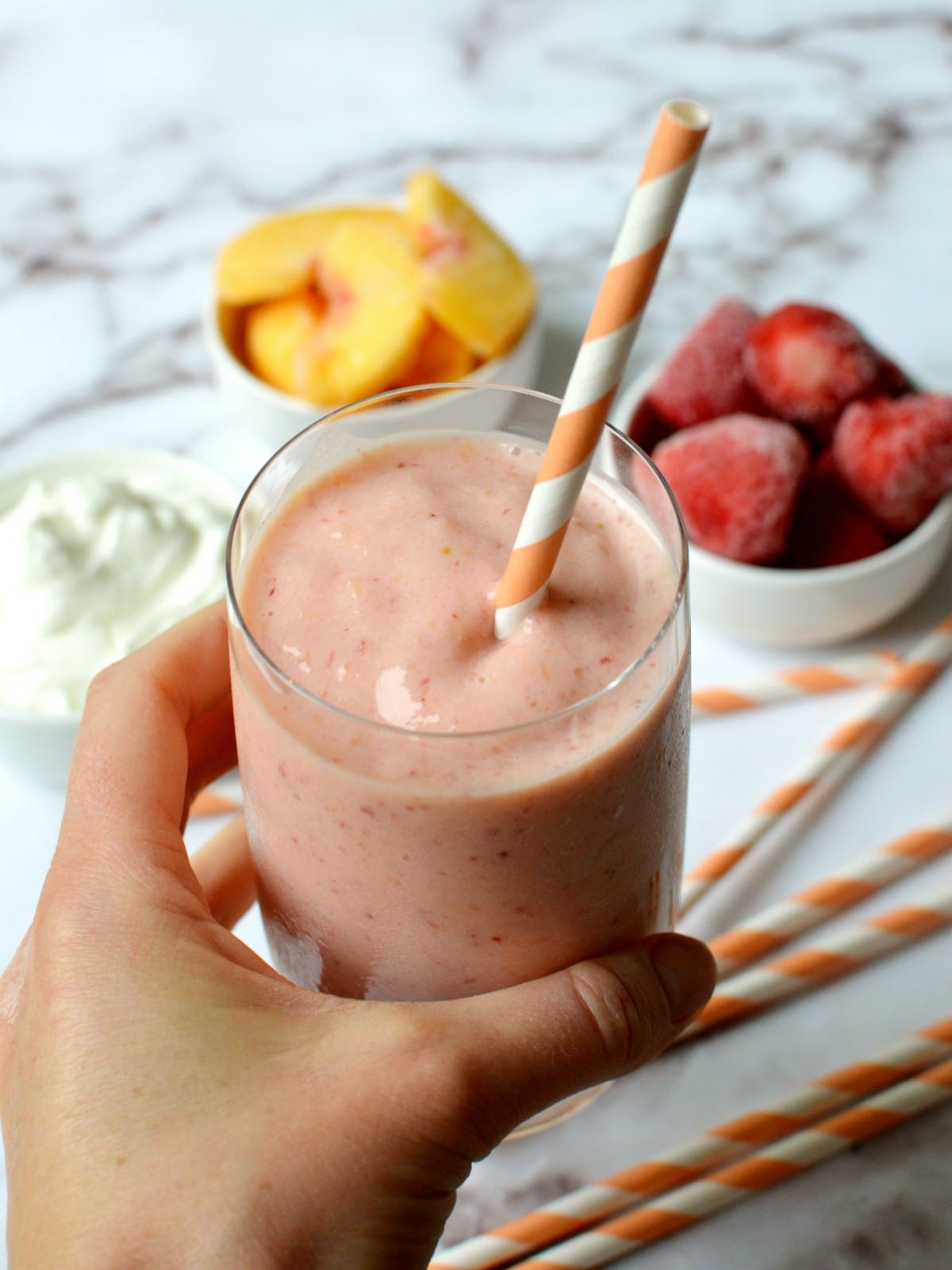 A strawberry peach smoothie with a straw