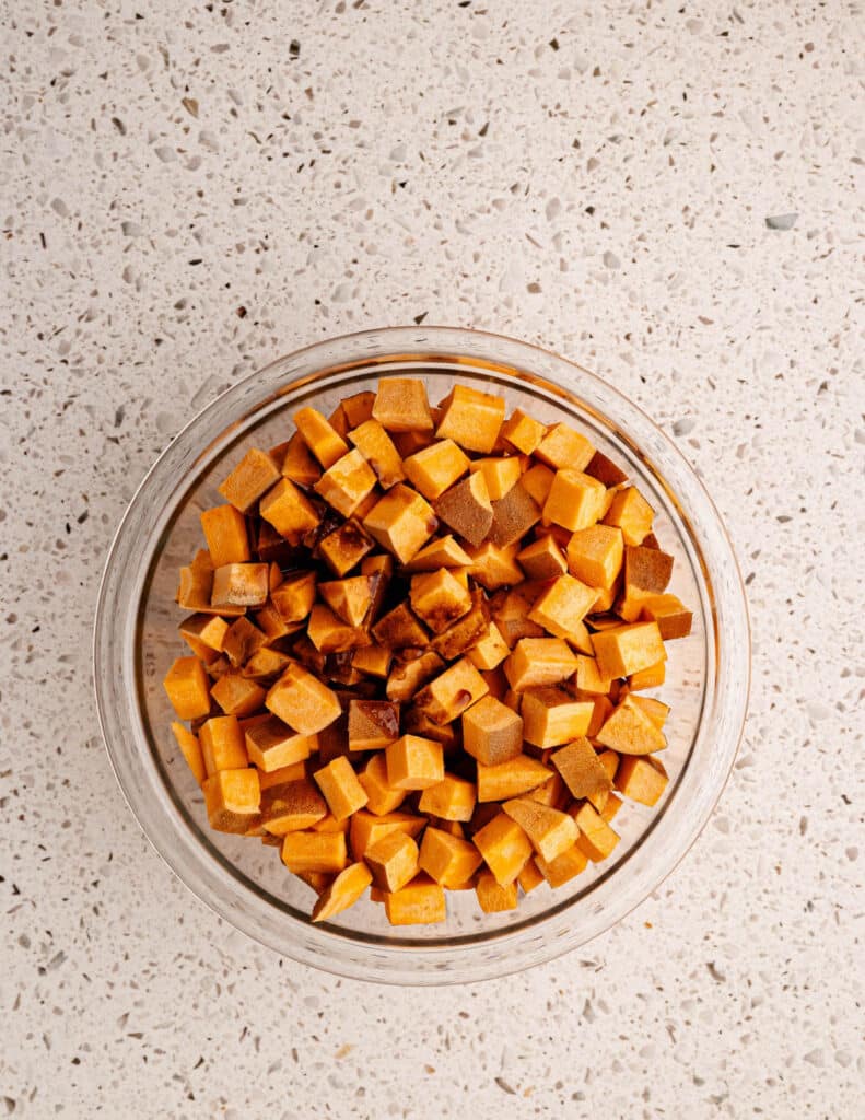 diced sweet potatoes in a bowl with cinnamon spiced coconut oil poured over it.