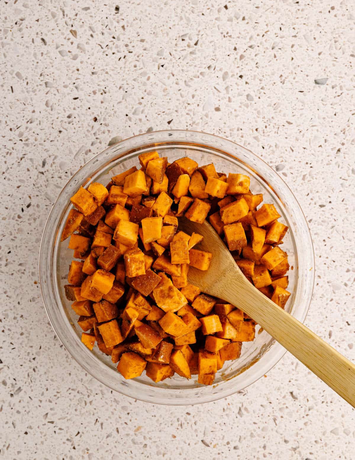 stirring diced sweet potatoes with cinnamon and coconut oil in a bowl.