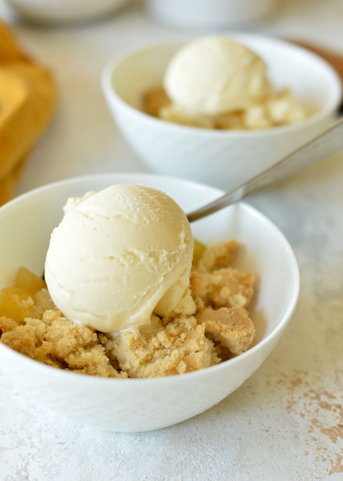 A delectable bowl of oat-free apple crisp topped with melting vanilla ice cream, ready to be enjoyed.
