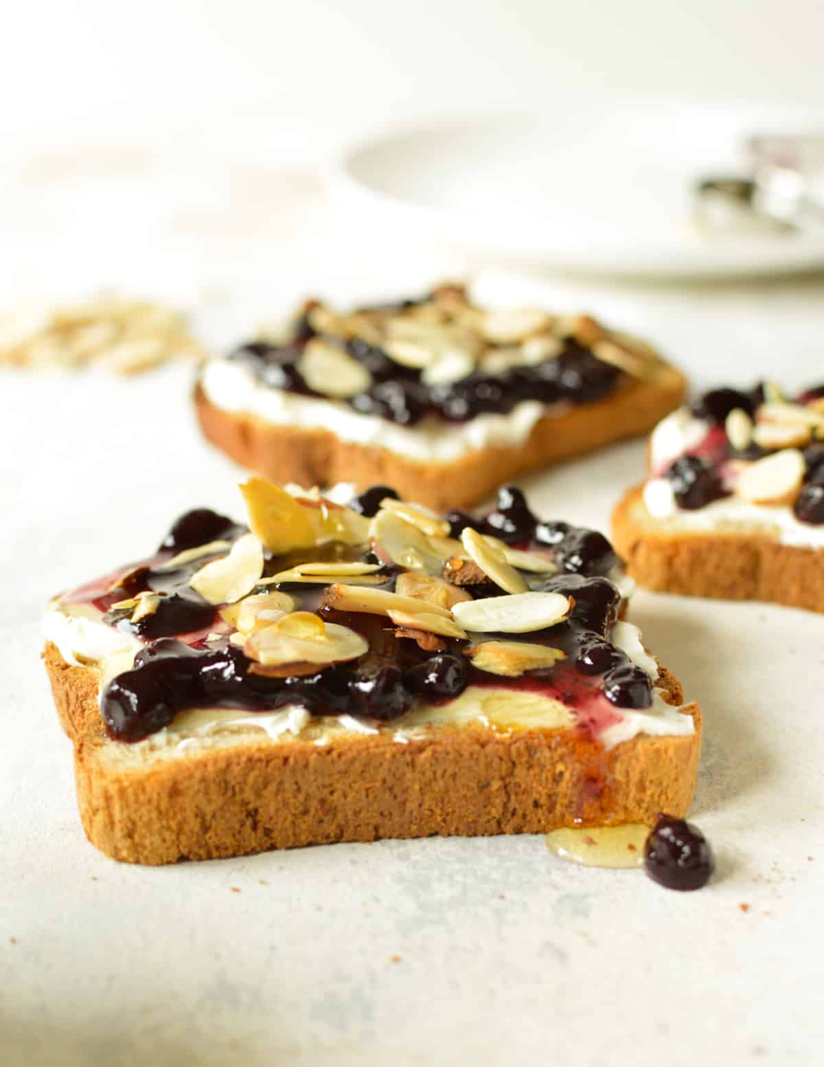 three pieces of toast with blueberry jam, cream cheese, and sliced almonds