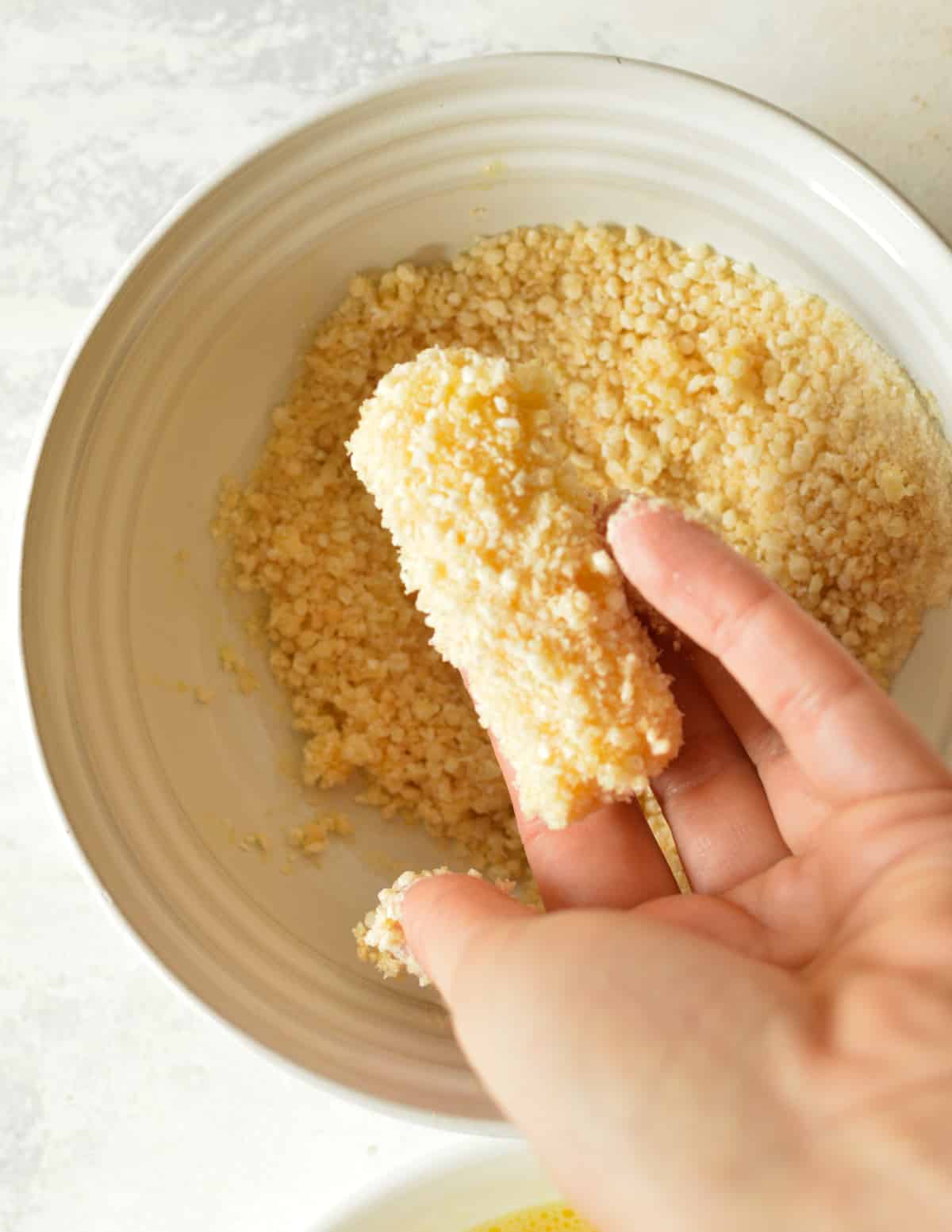 hand holding a cheese stick coated in gluten free breadcrumbs