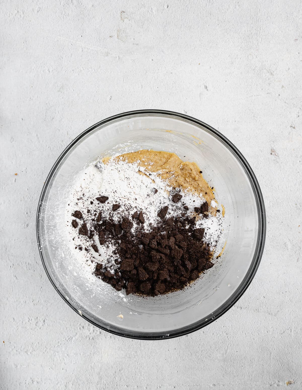 creamed butter and sugar in a bowl with dry ingredients and Oreo cookie crumbs on top.