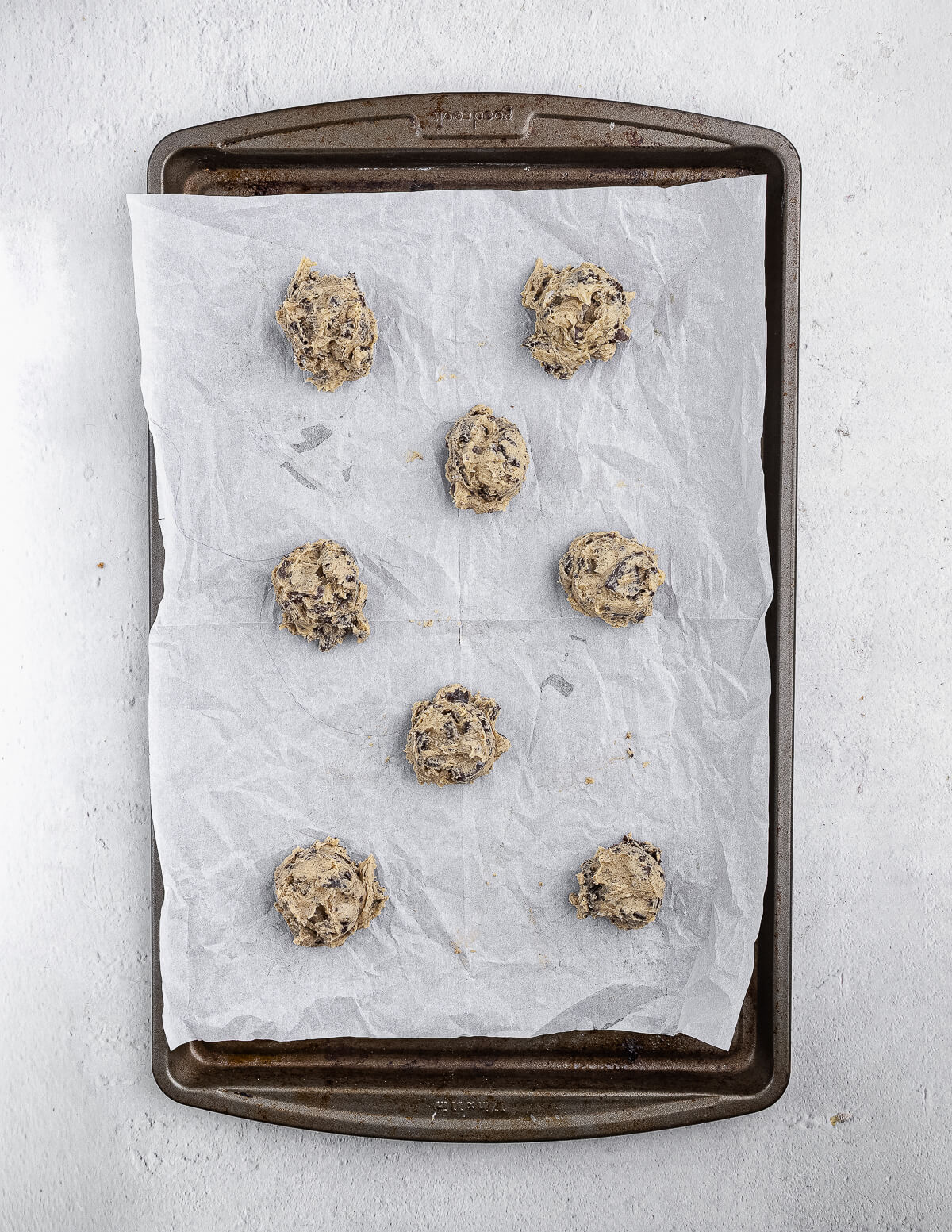 Chocolate chip Oreo cookie dough balls on a parchment lined sheet pan.