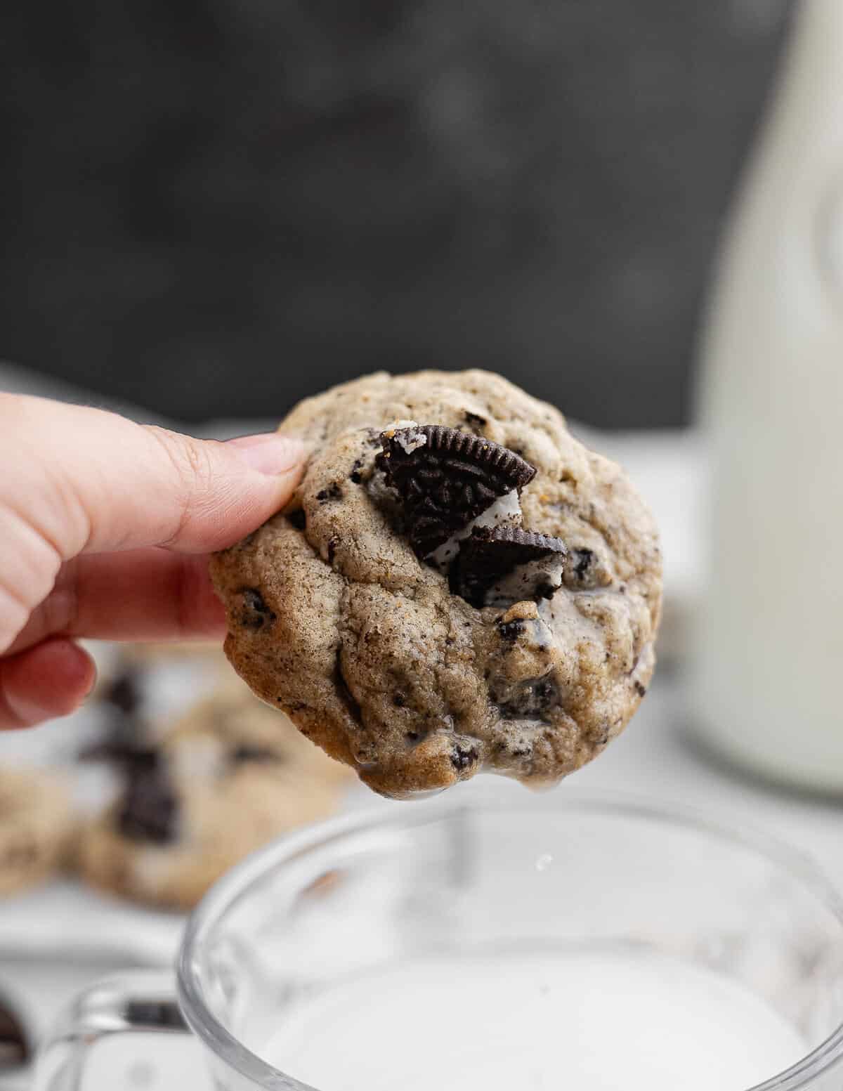 hand holding an Oreo chocolate chip cookie above a glass of milk.