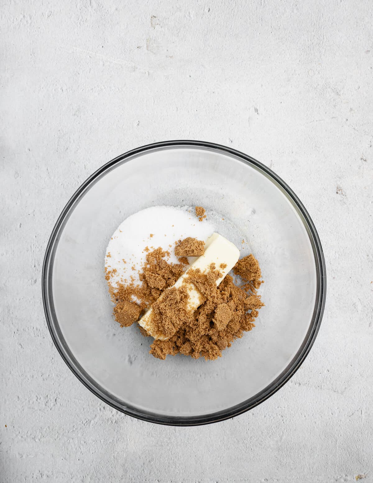a stick of butter, sugar, and brown sugar in a bowl.