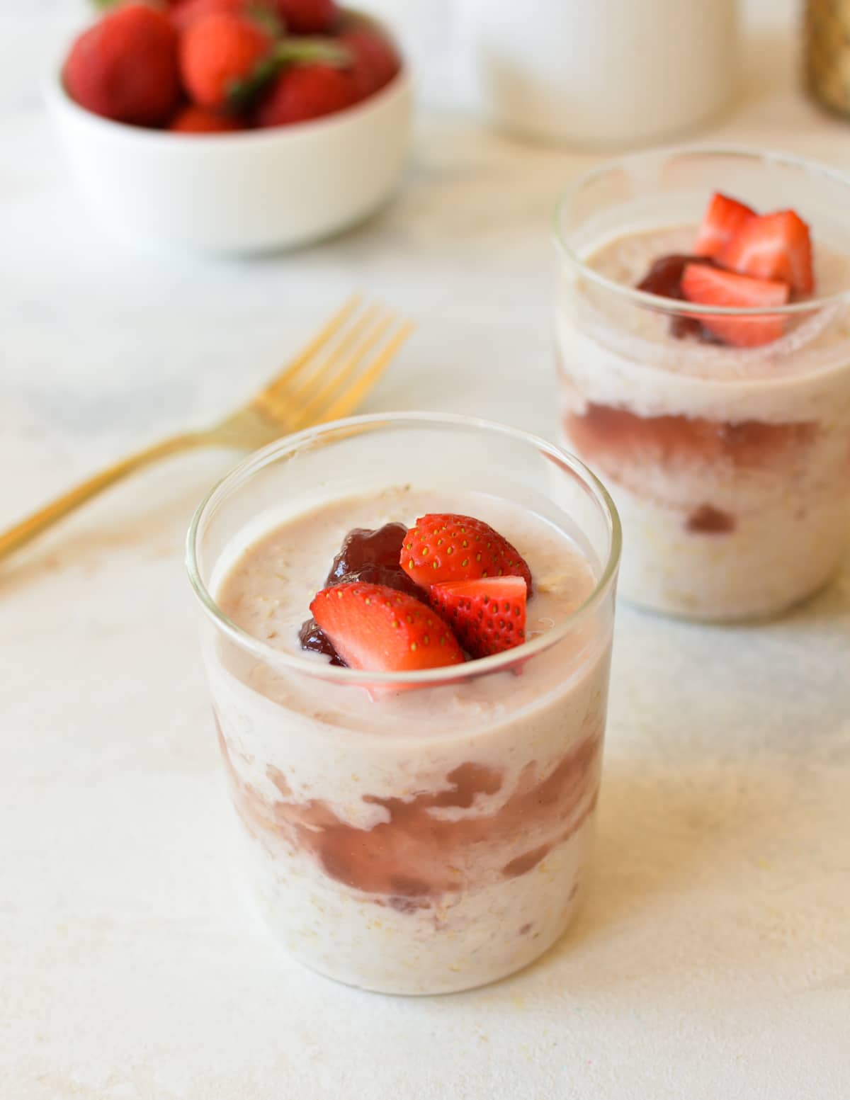 two glasses with overnight oats, jam, and berries