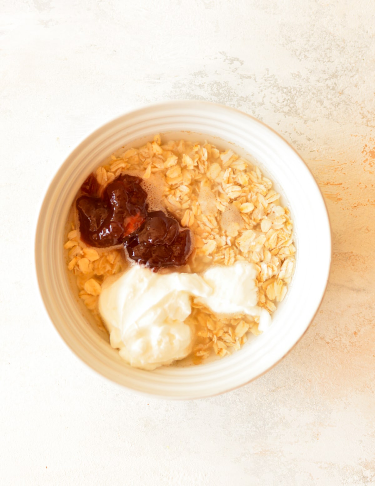a bowl of oats with water, yogurt, jam, and maple syrup