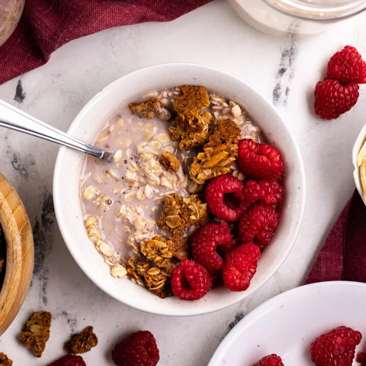 a bowl of overnight oats with raspberries and granola on top.