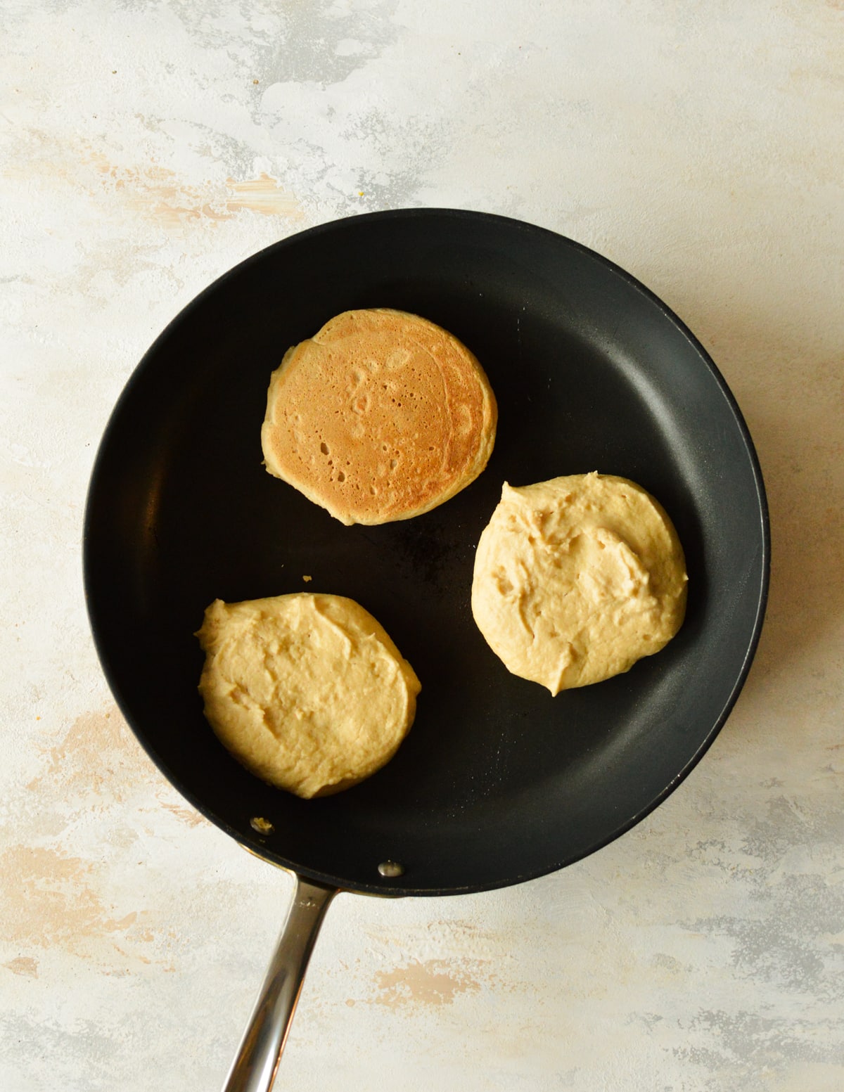 three pancakes cooking in a skillet