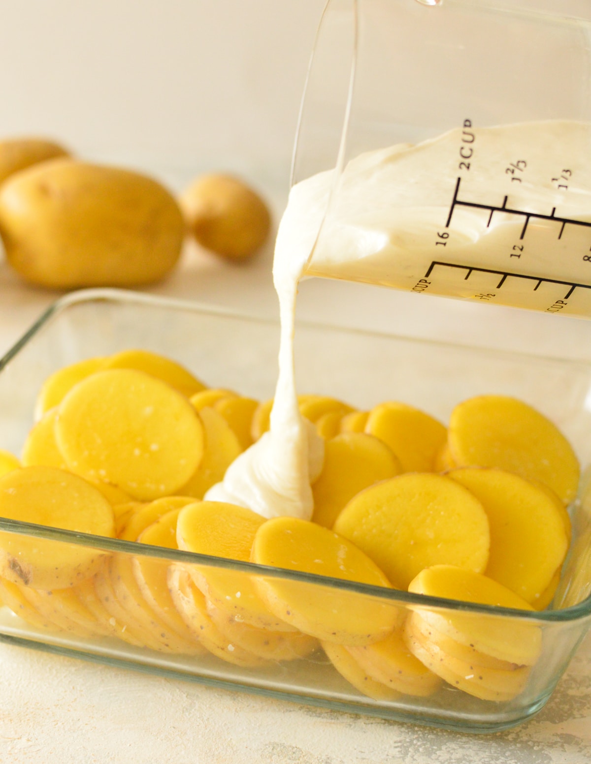 pouring gluten free bechamel onto potatoes