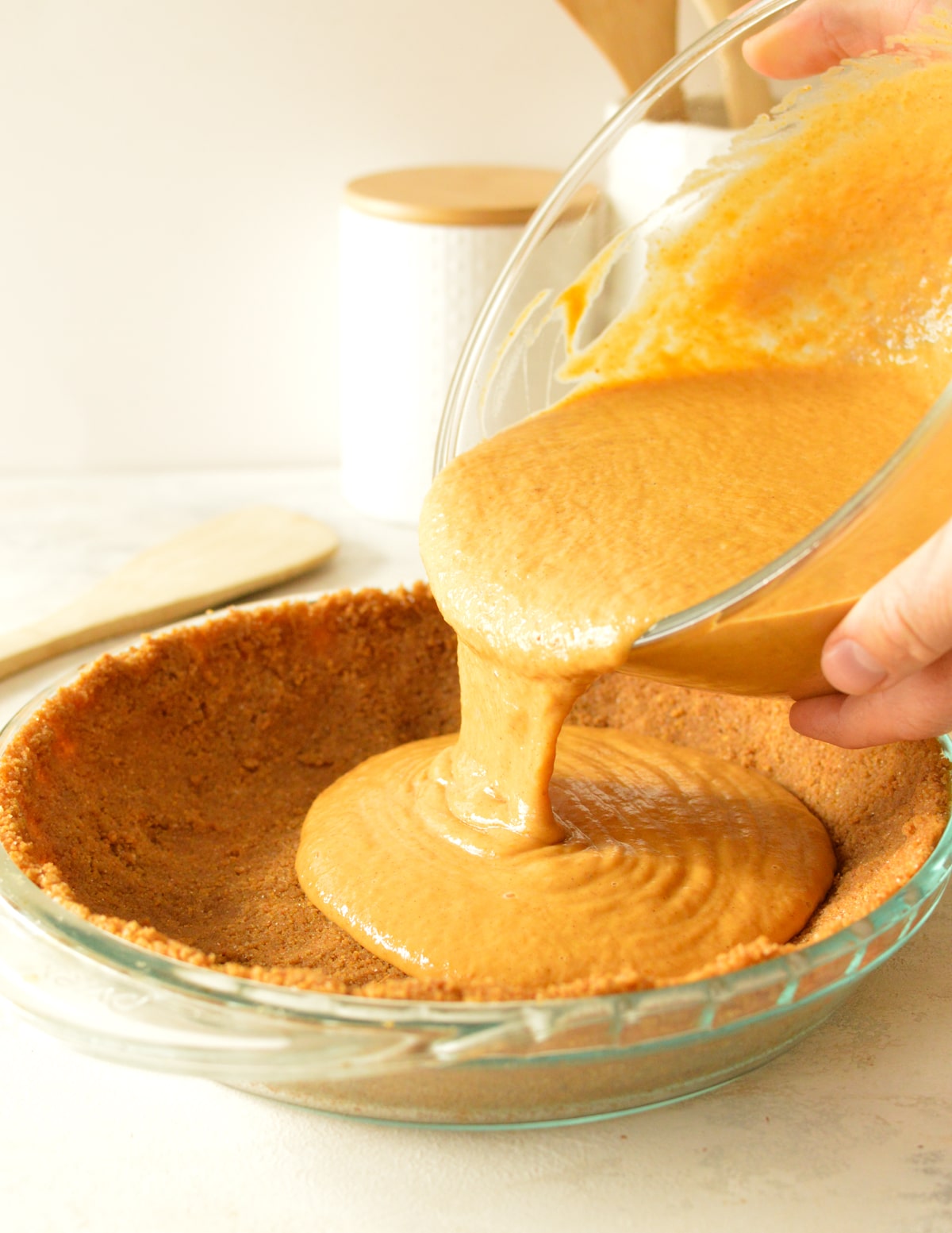 hands pouring pumpkin pie batter into crust