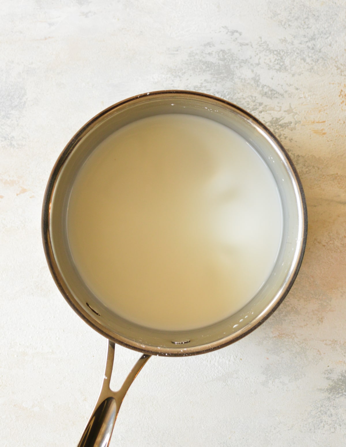 A small saucepan with water and cornstarch being stirred to create a lump-free slurry, the first step in making strawberry cake filling.