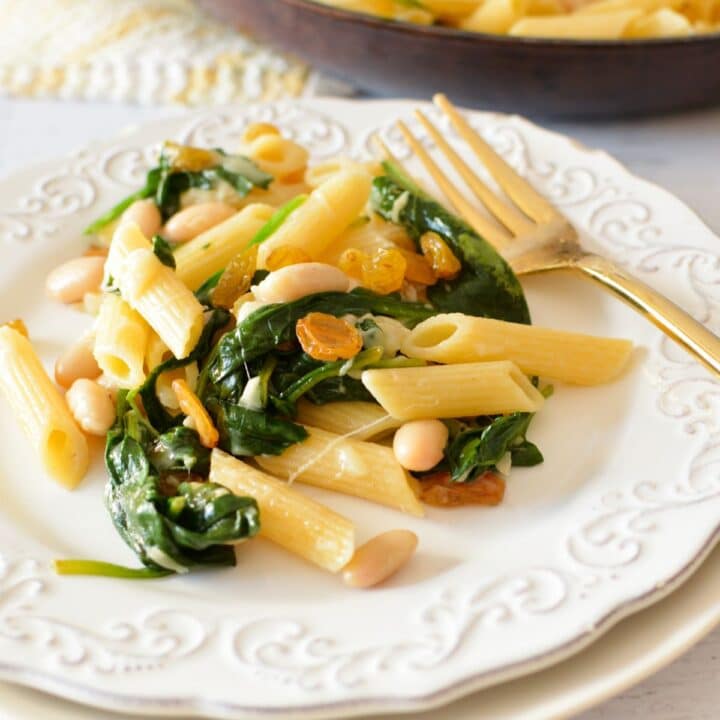 a plate of pasta with spinach, raisins, and white beans.