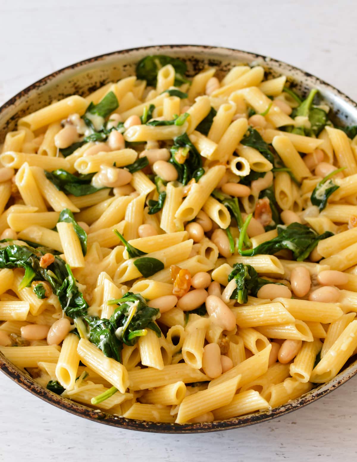 a skillet with pasta, spinach, white beans, and raisins.