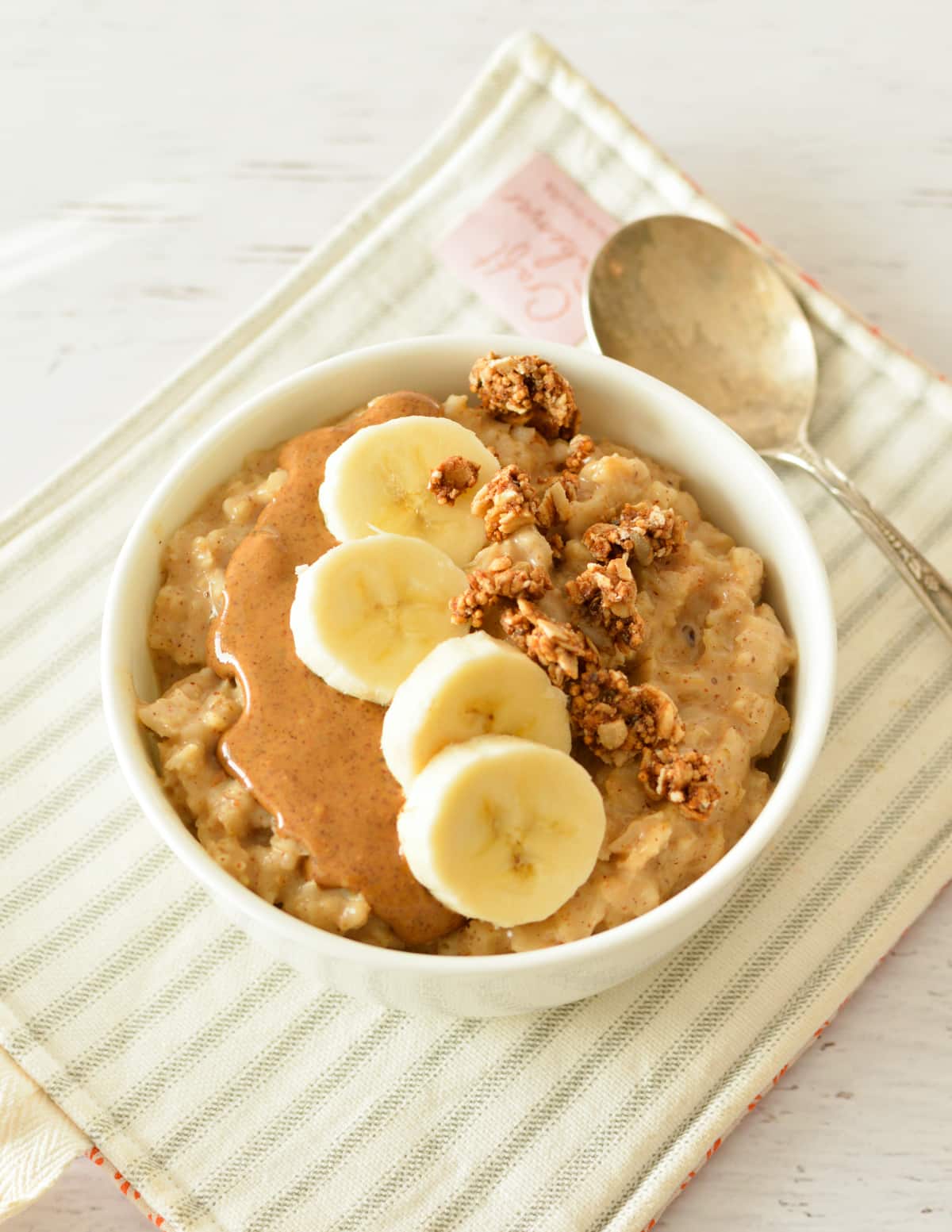 a bowl of oatmeal with almond butter, bananas, and granola.