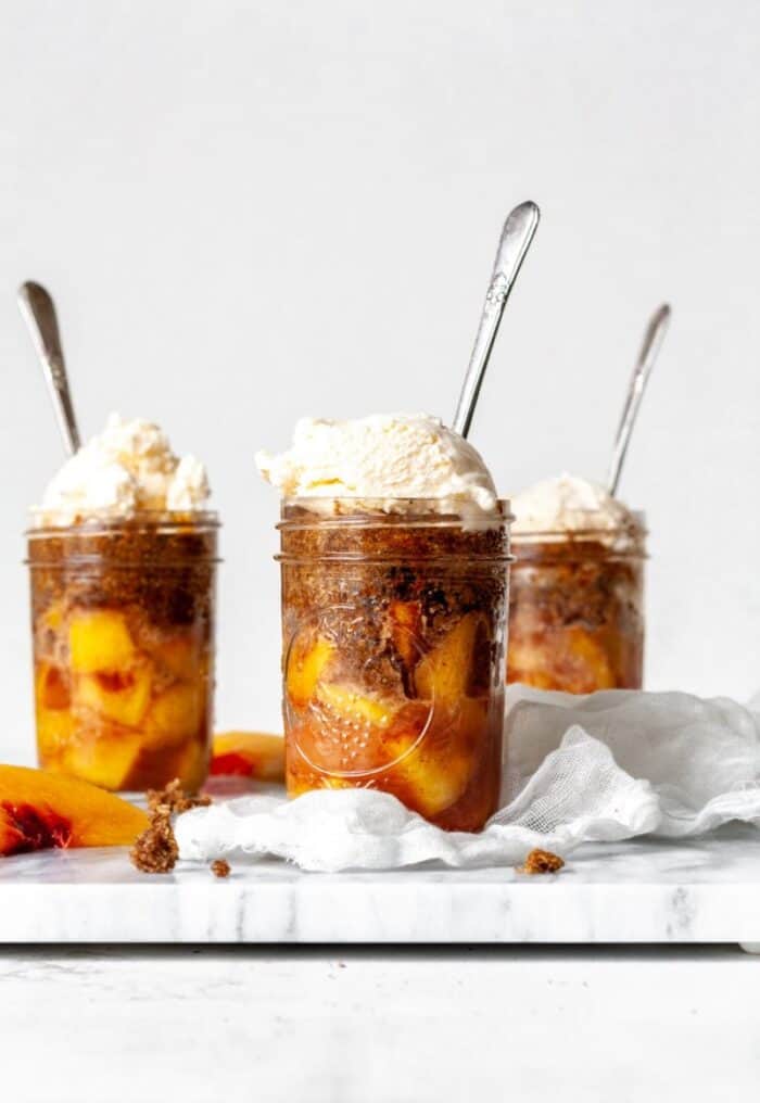 peach cobblers in jars with vanilla ice cream and spoons.