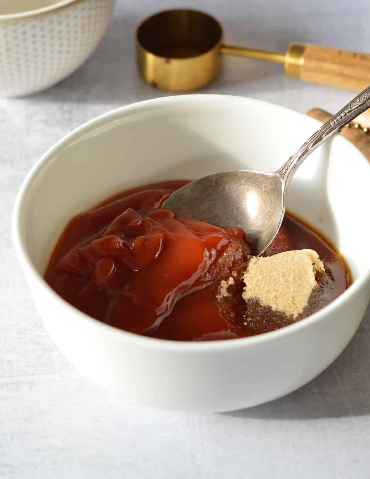 a bowl with ketchup, brown sugar, and a spoon in it.