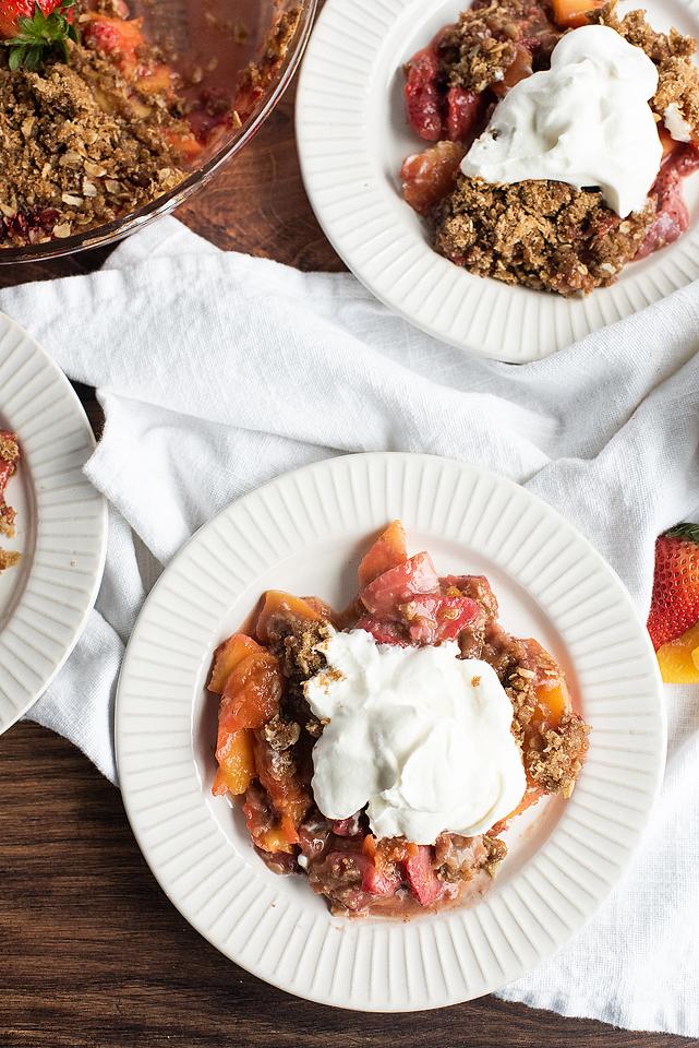 two plates of strawberry peach crisp with whipped cream.