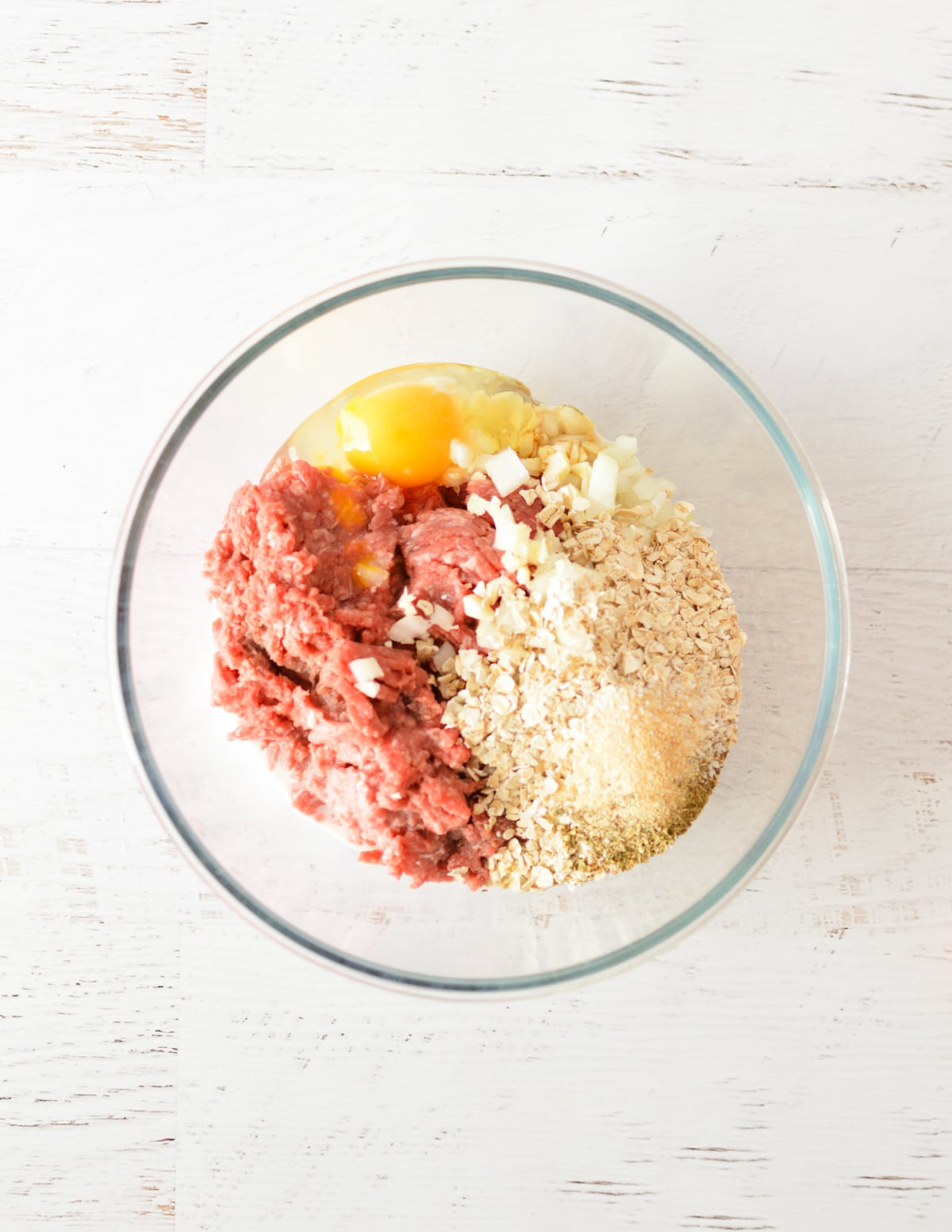a bowl of ground beef, egg, oats, spices, and onion.