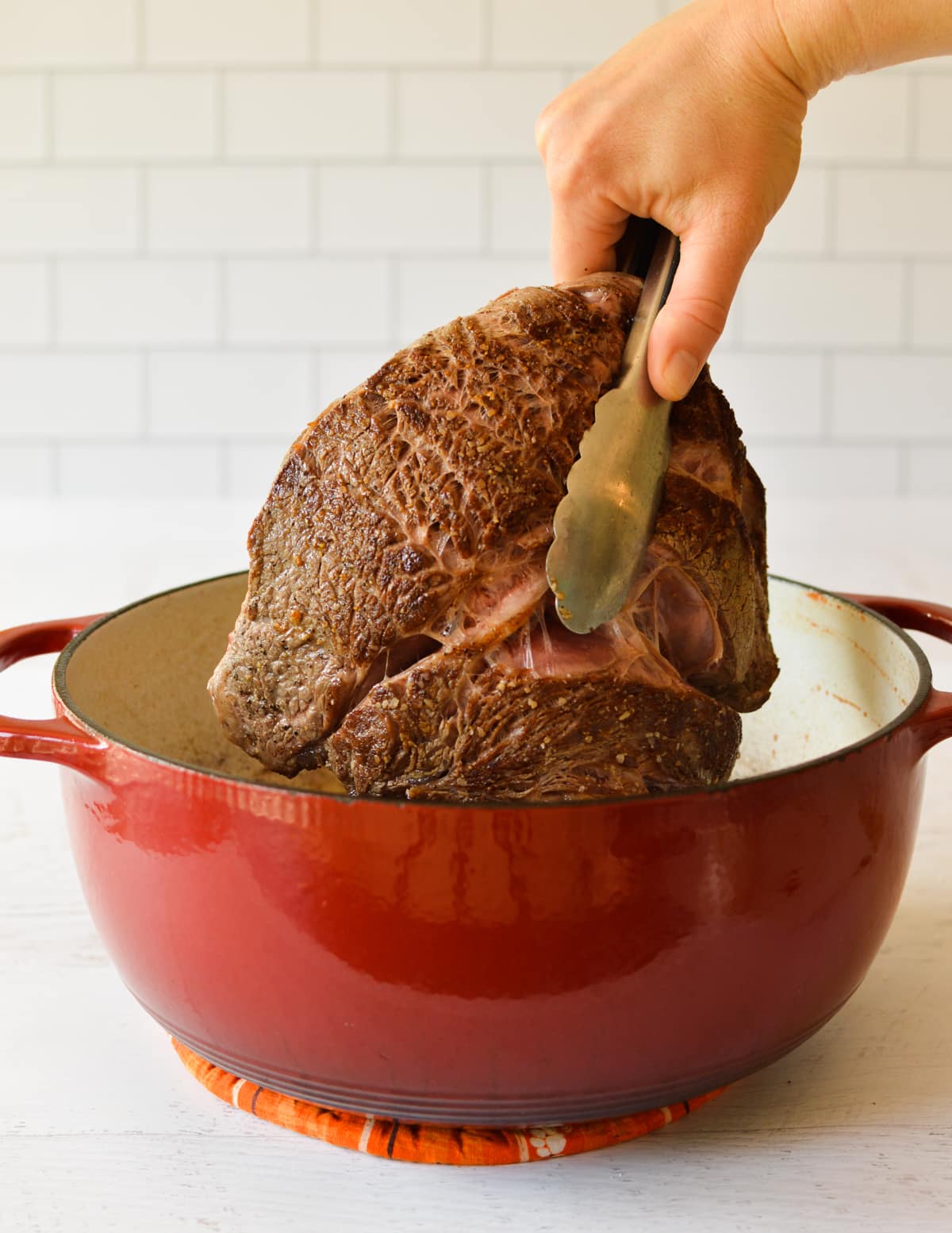 tongs holding chuck roast in pot.