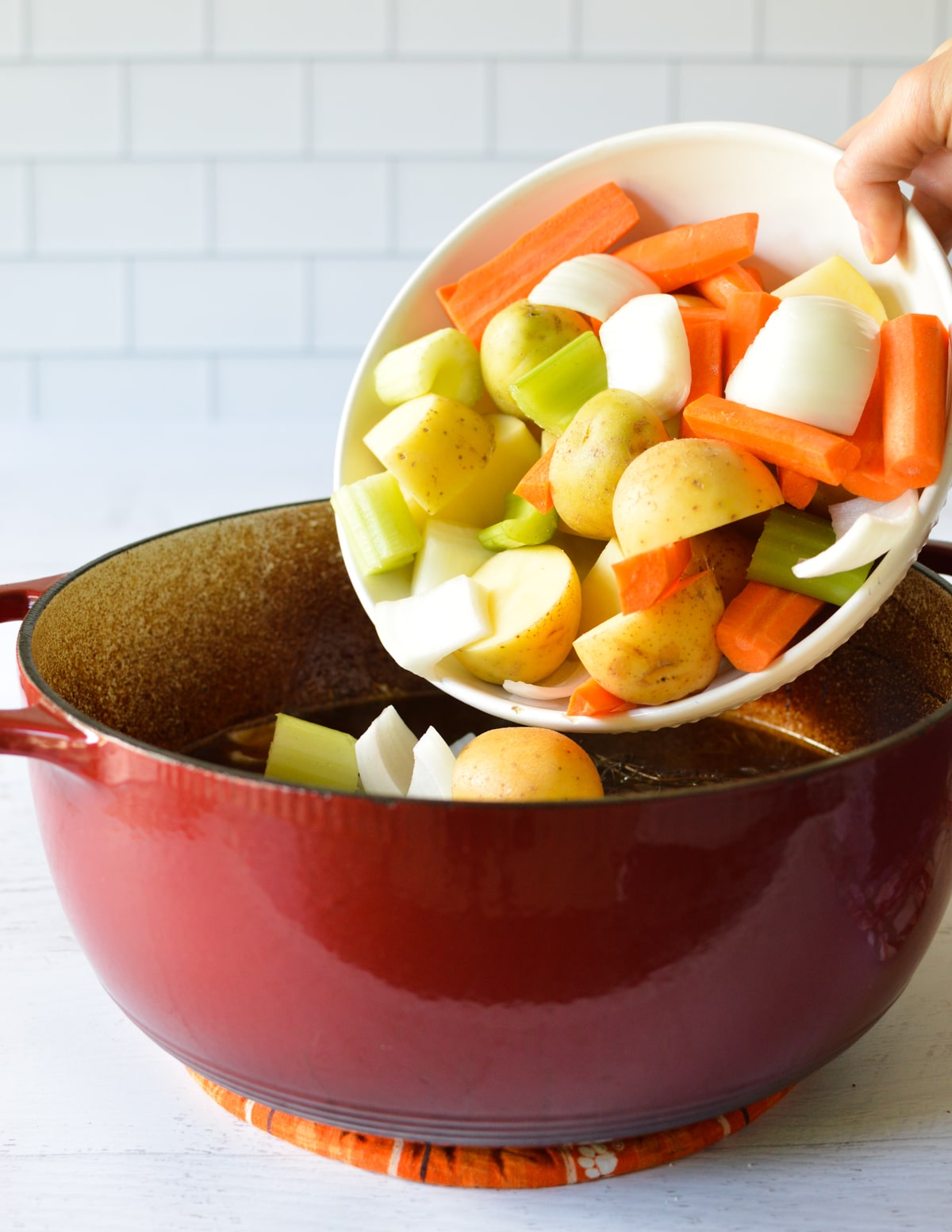 pouring a bowl of veggies into a dutch oven.