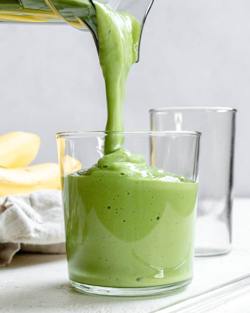 pouring a banana kale smoothie into a glass.